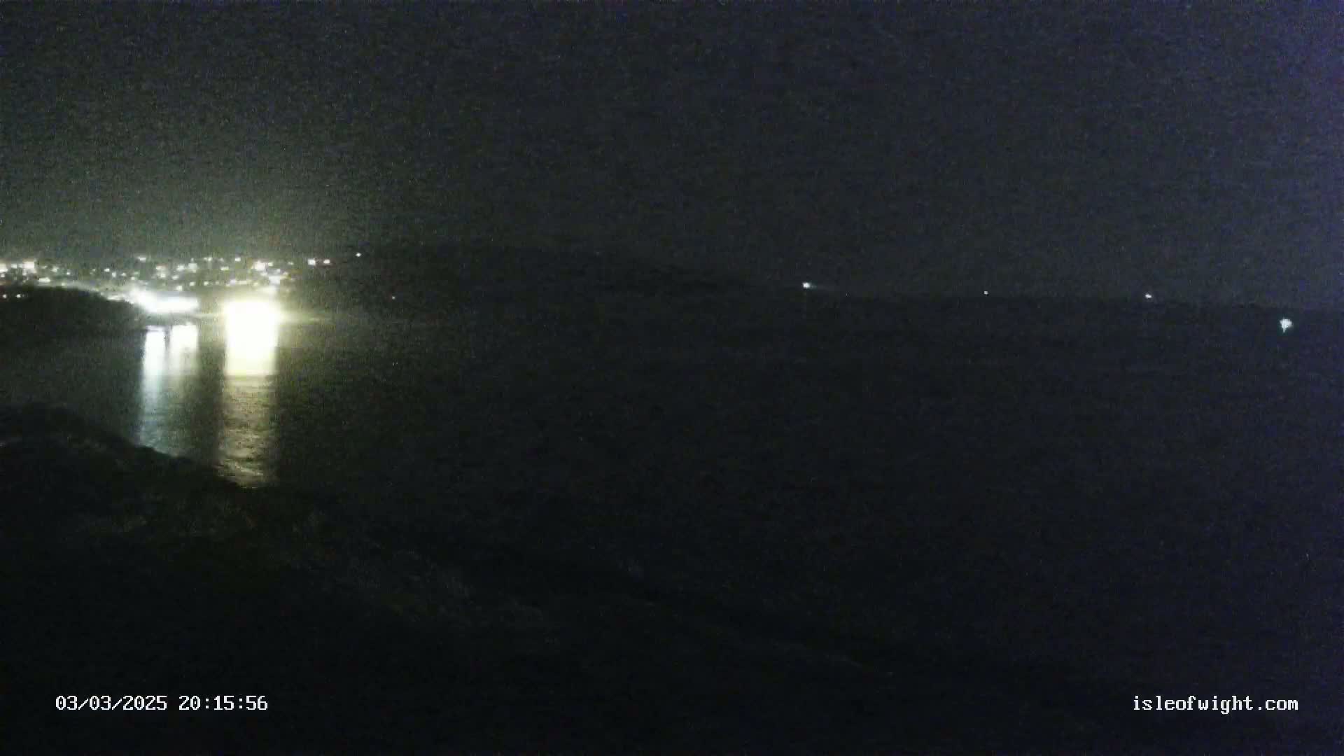A nighttime view of a body of water reflecting the lights of a city in the distance, under a dark sky.