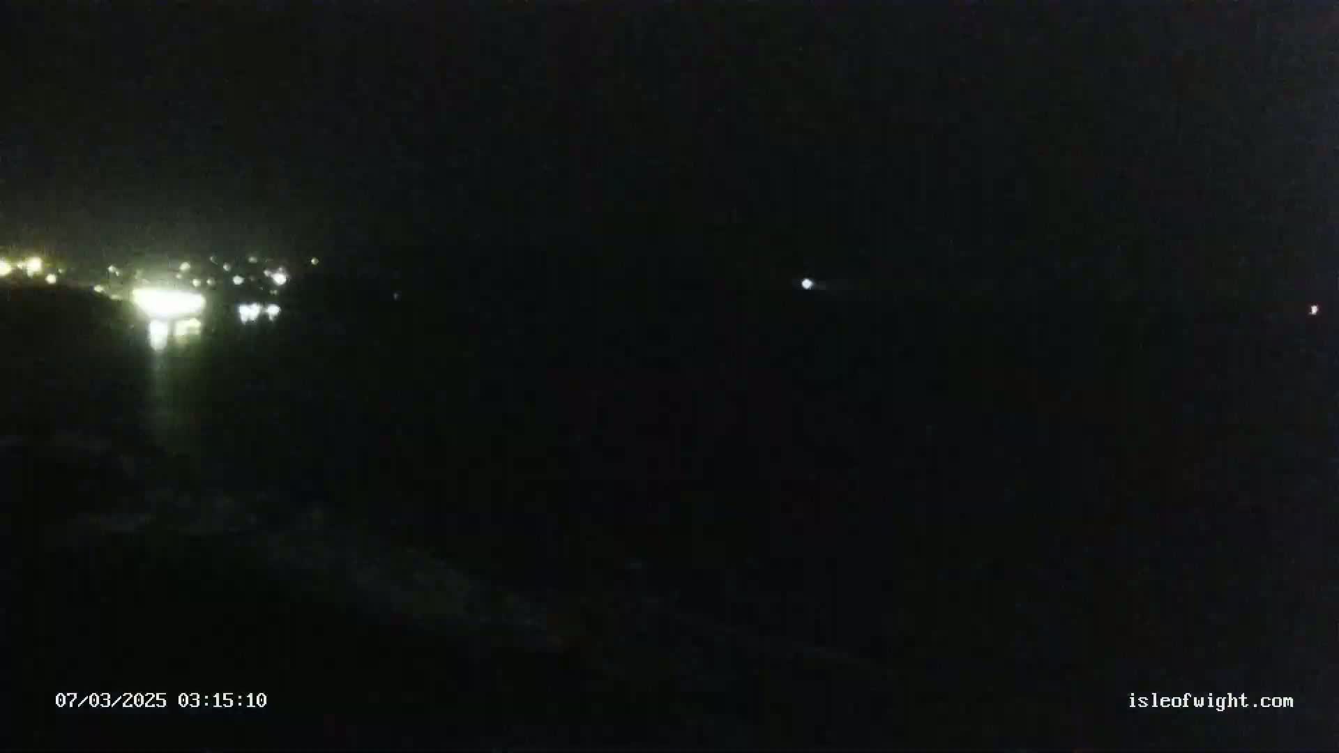 A nighttime long shot shows a dark landscape with distant, faint lights from a town or city.