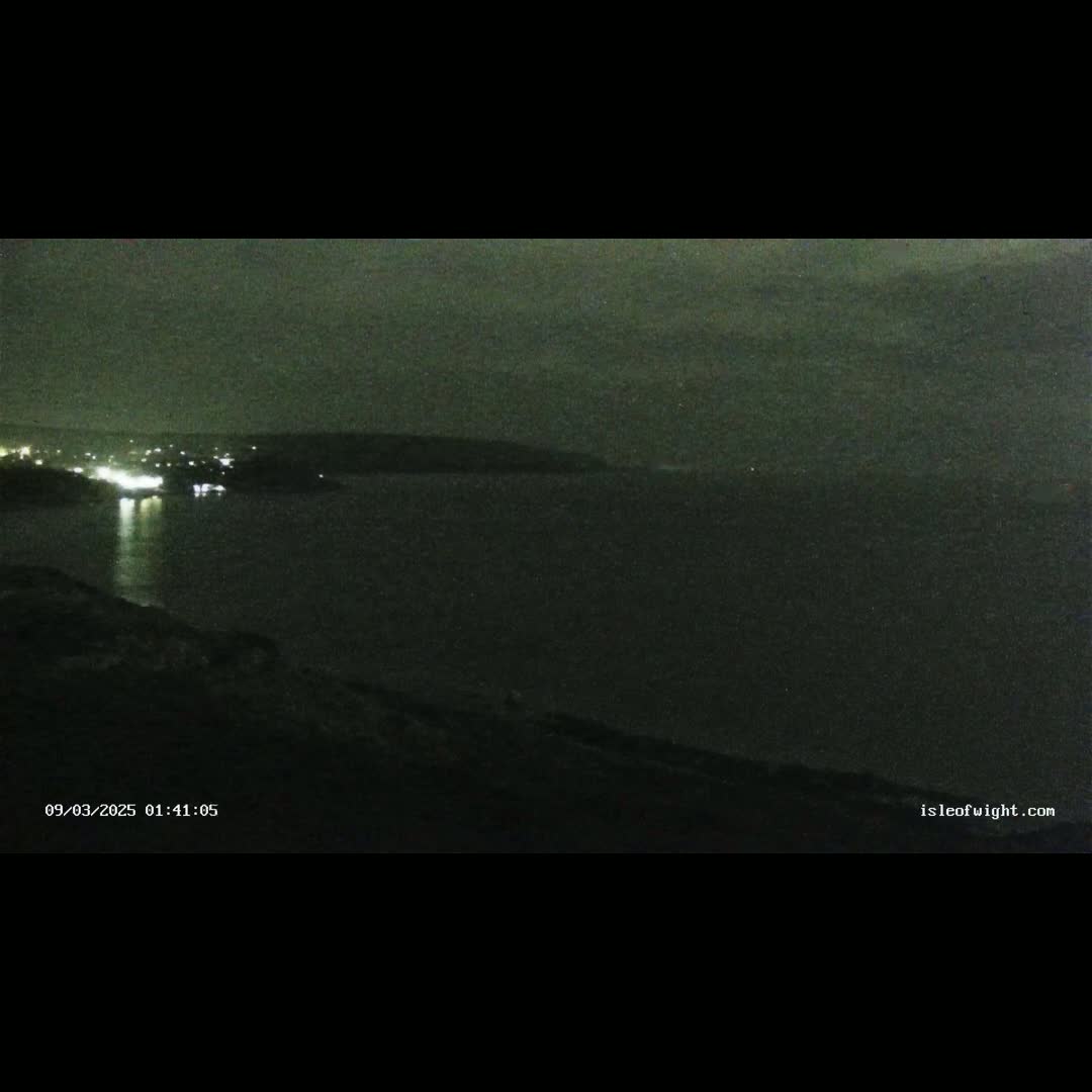 A nighttime, low-light view of a dark body of water with a distant shoreline showing faint lights.