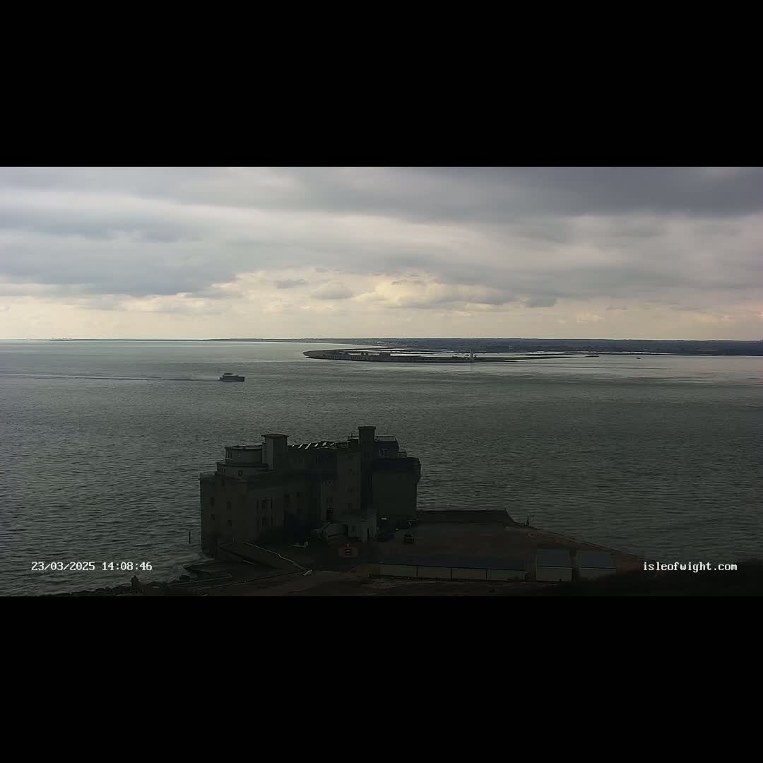 A castle-like structure sits on the shore of a body of water under a cloudy sky, with a small boat visible in the distance.