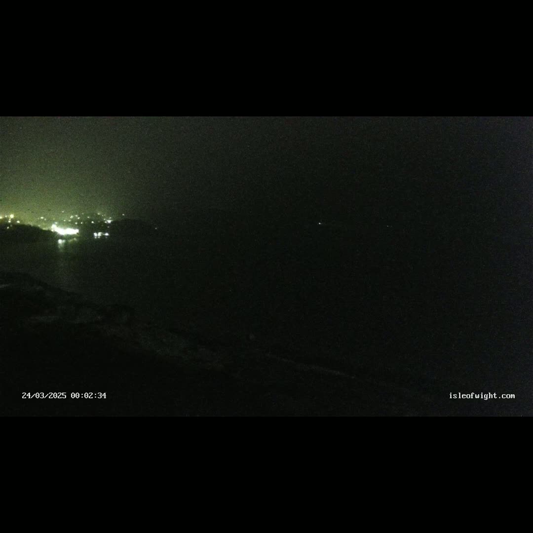 A nighttime, dark view of a distant shoreline with faint lights visible across the water.