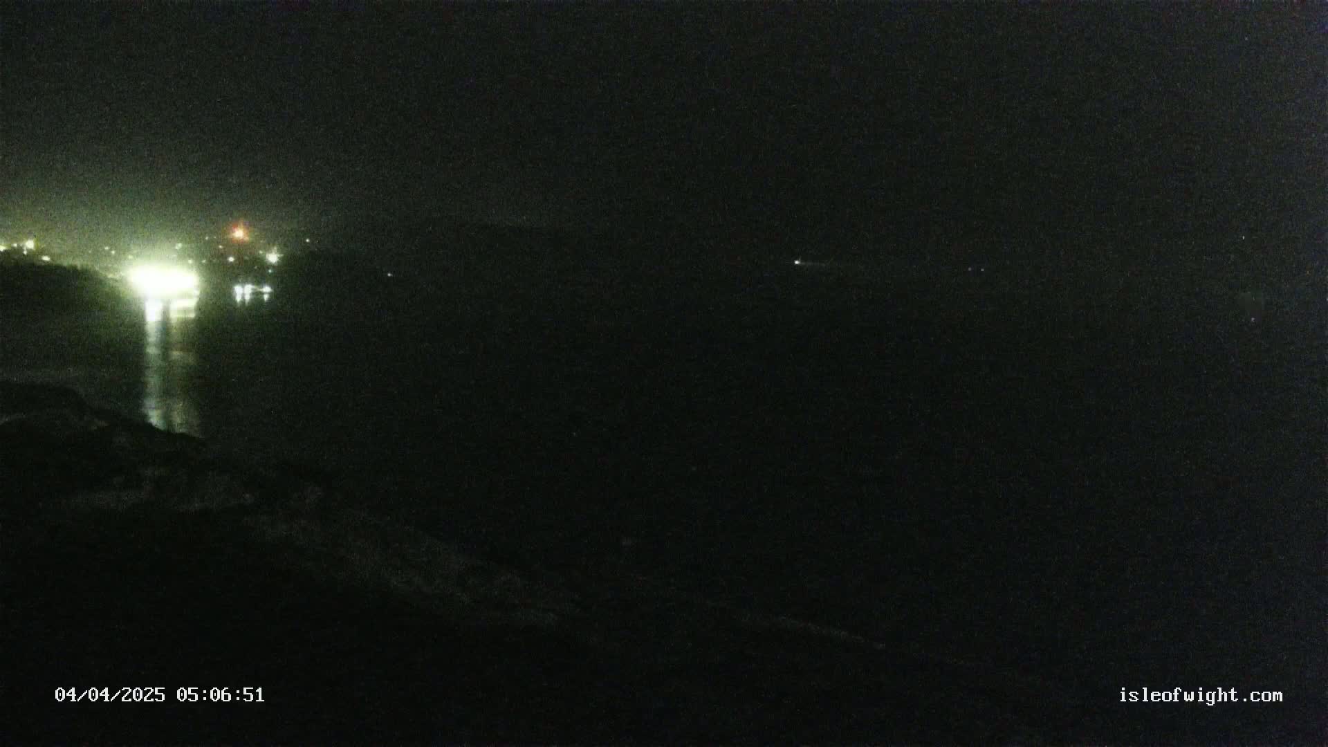 A dark, nighttime view of a body of water reflecting distant lights, under a clear, dark sky.