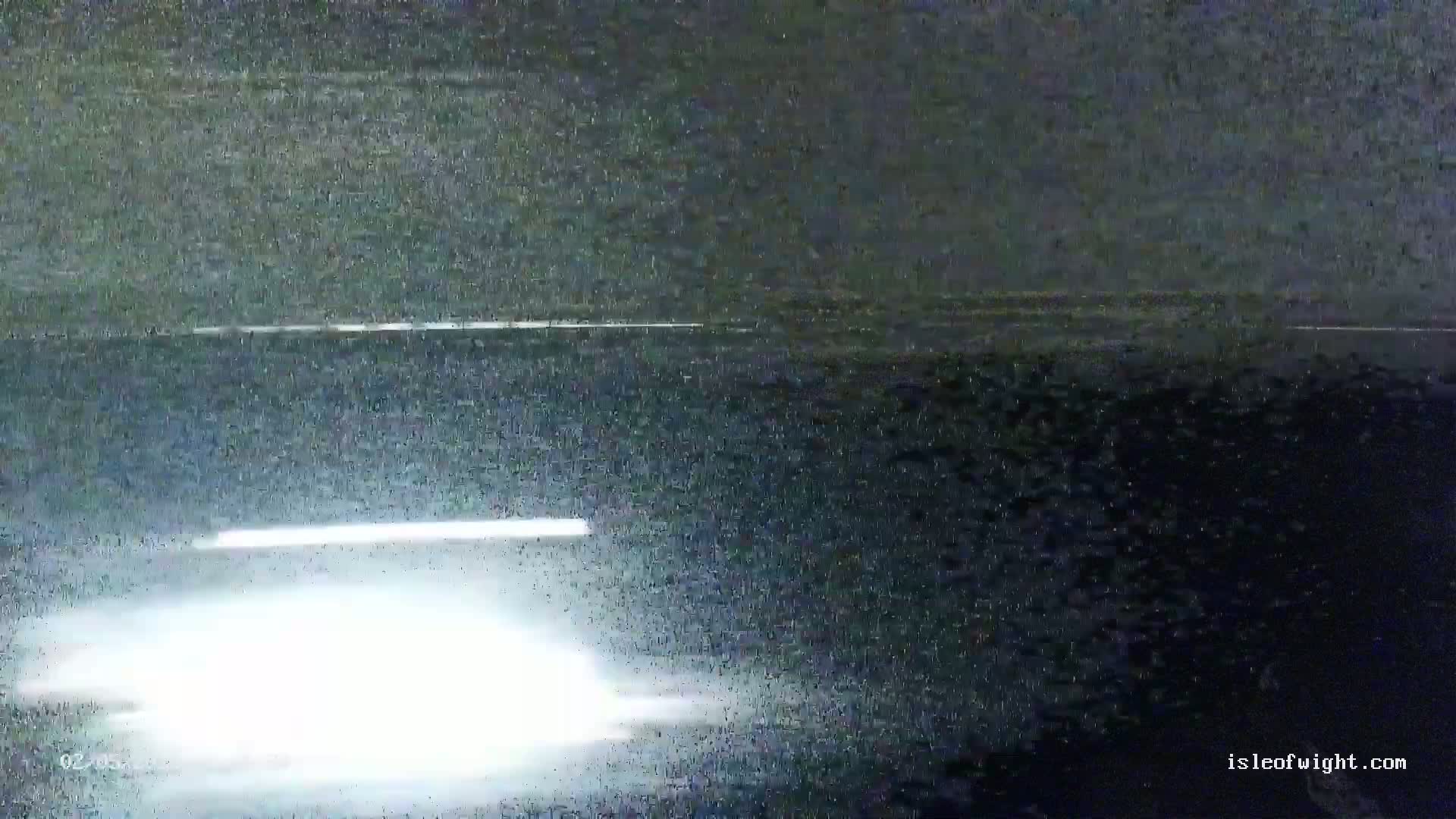 A low-quality, nighttime image shows a bright light source on a dark road with heavy static interference.