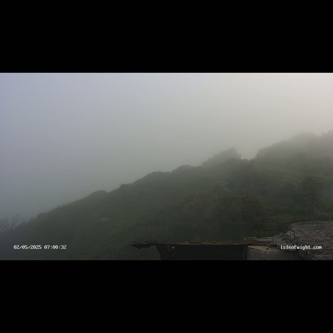A foggy morning obscures a dark green hillside partially visible behind a low stone wall.