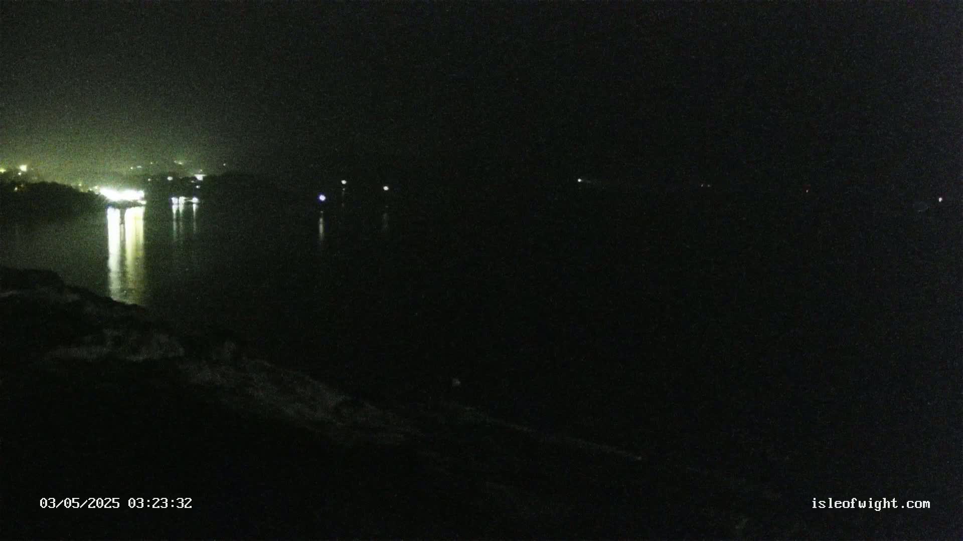 A dark nighttime view of a body of water reflecting distant lights from a shoreline.