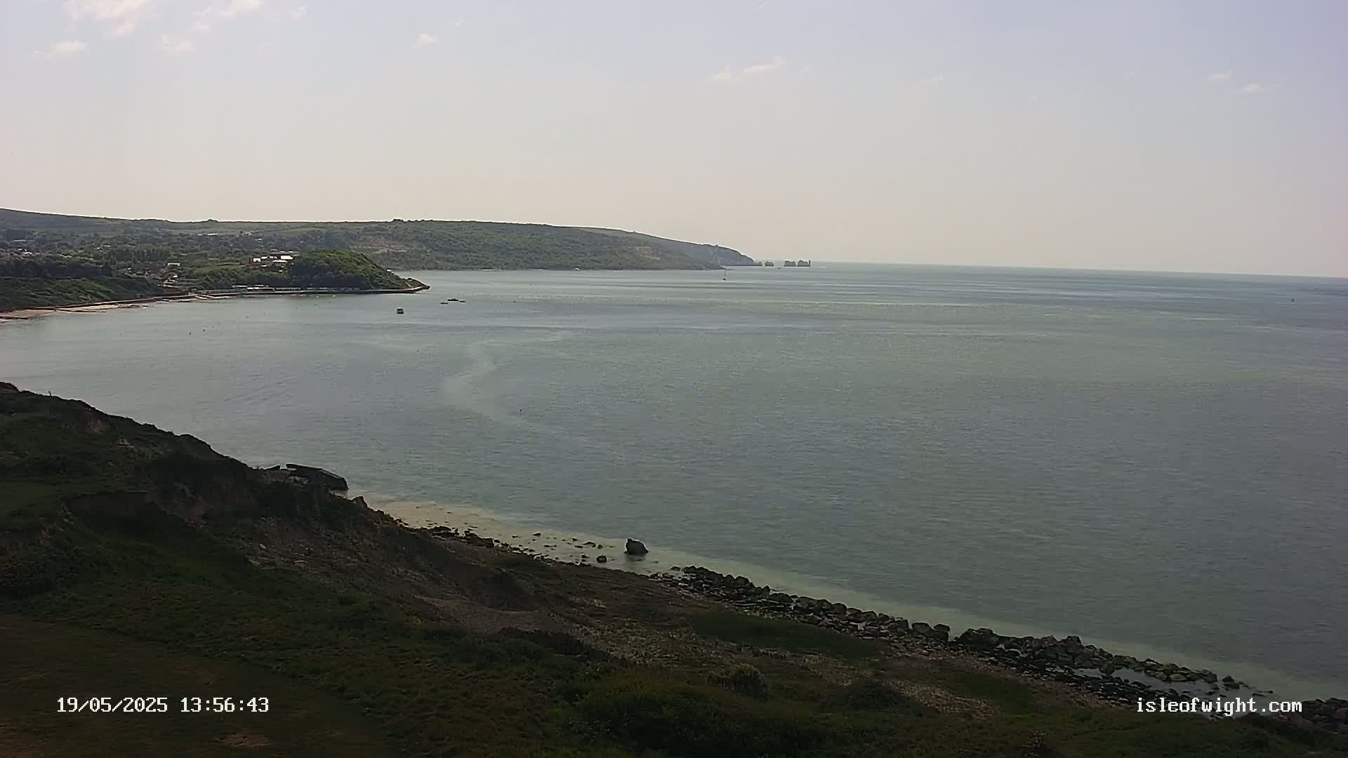 A calm, gray sea stretches to a distant, tree-covered headland under a mostly clear sky.