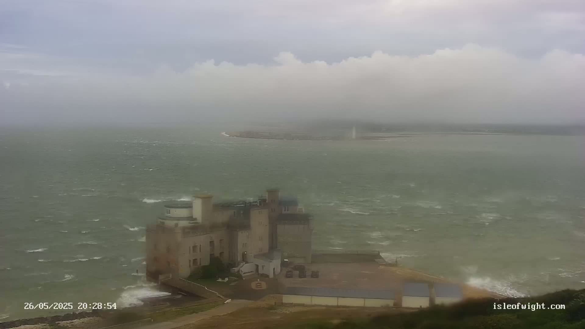 A coastal castle is shown under an overcast sky with a choppy sea.