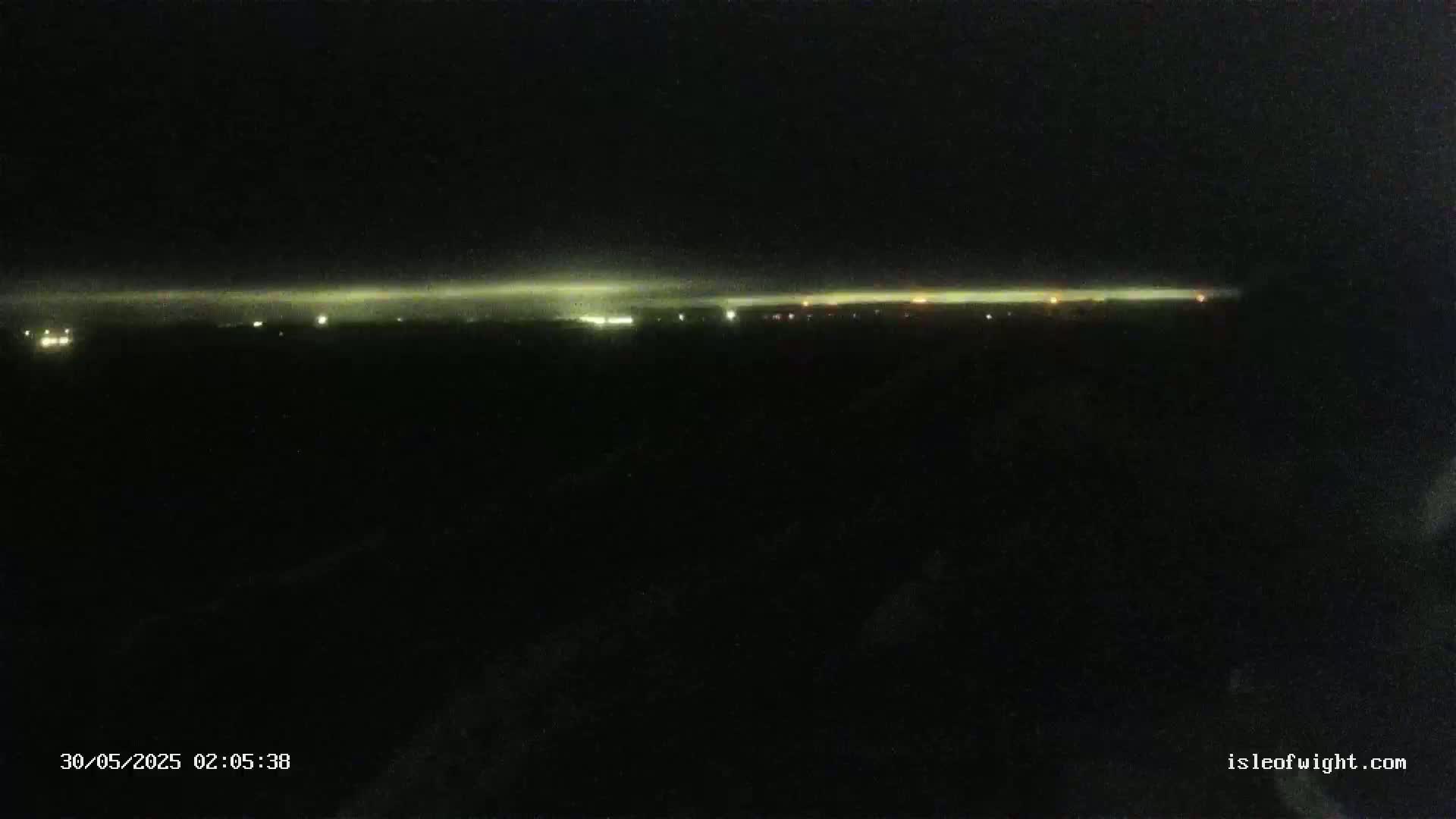 A nighttime, long shot of a faintly lit horizon with a few scattered lights visible in the distance.
