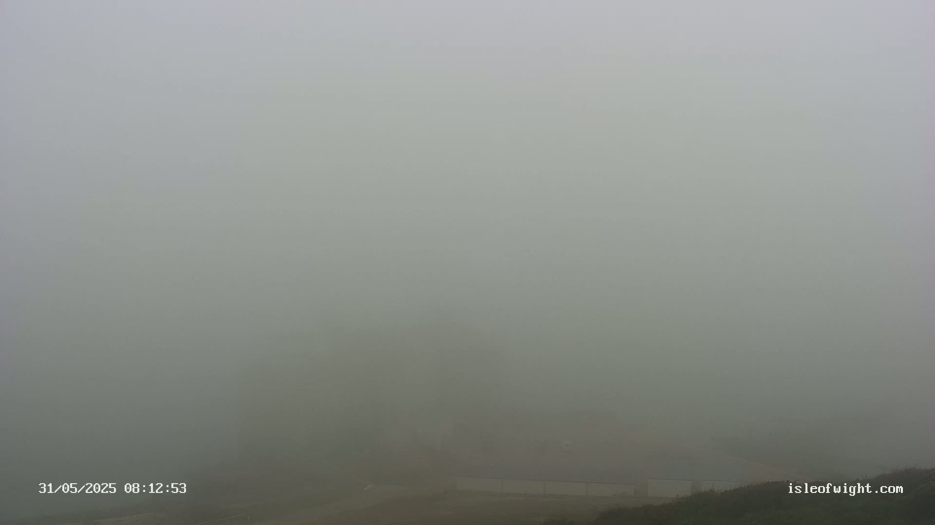 A foggy landscape shows a low-lying structure partially obscured by heavy fog.
