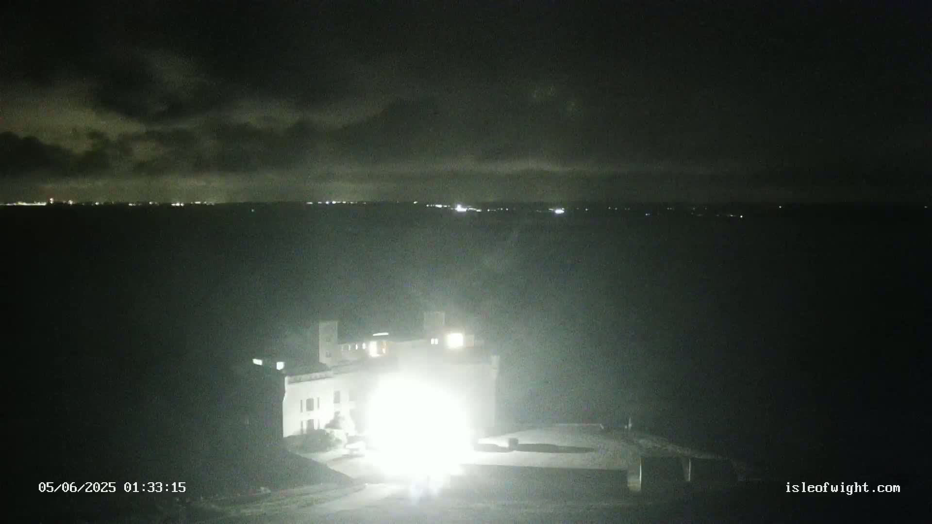 A brightly lit building stands out against a dark, cloudy night sky, with a distant line of lights visible on the horizon.