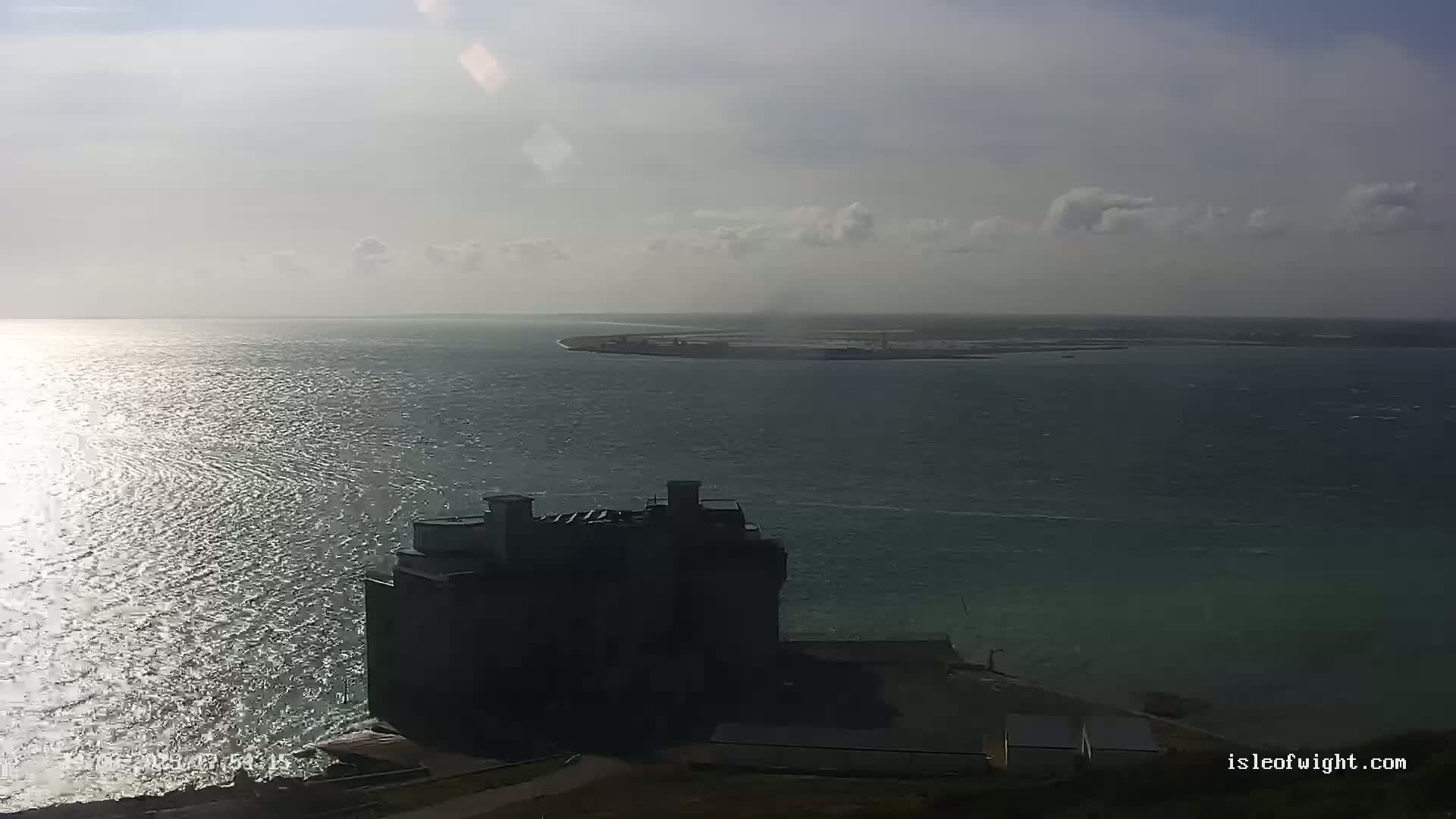 A dark building sits on a coast overlooking a body of water under a partly cloudy sky.
