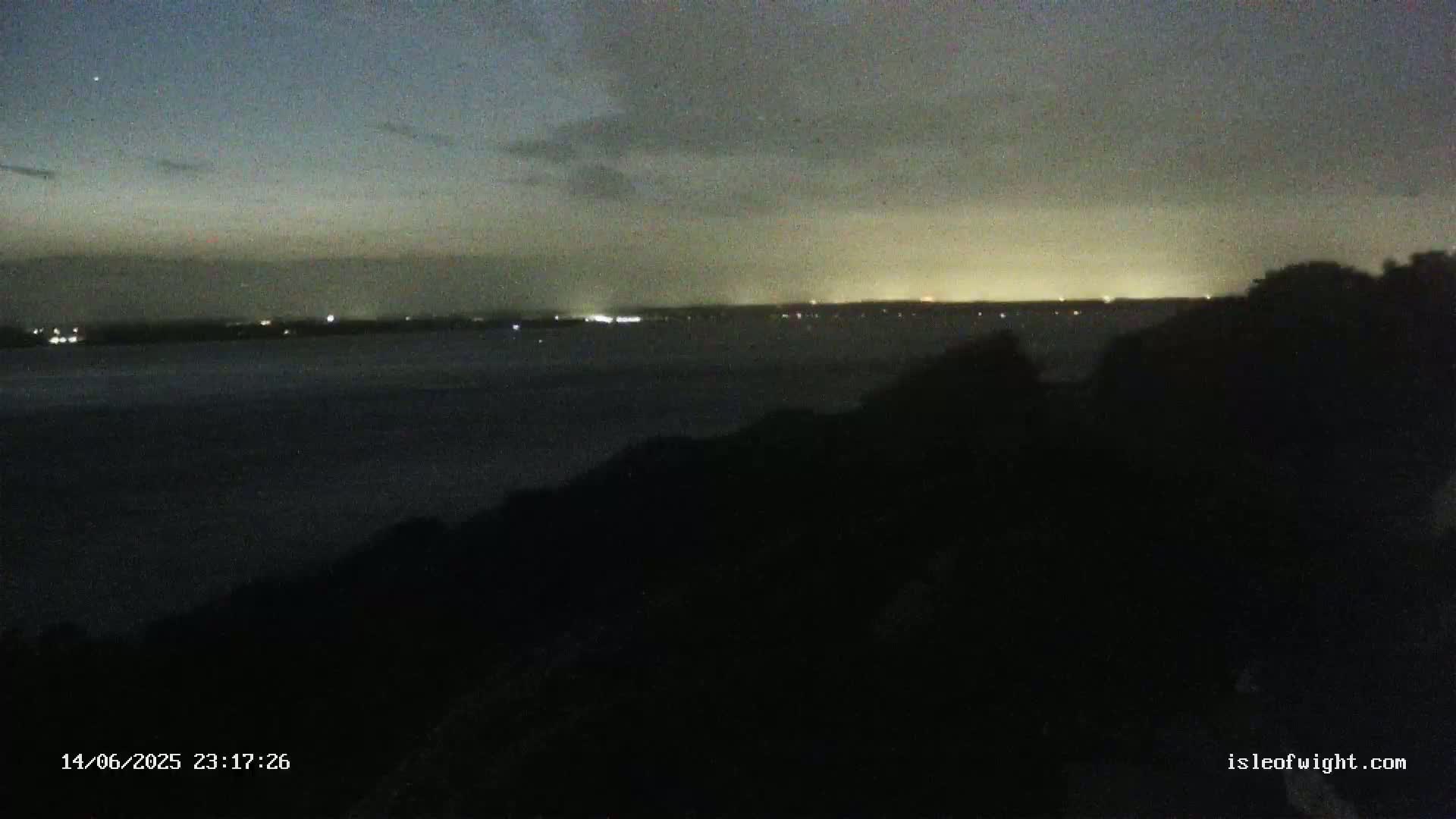 A dark building sits on a coast overlooking a body of water under a partly cloudy sky.