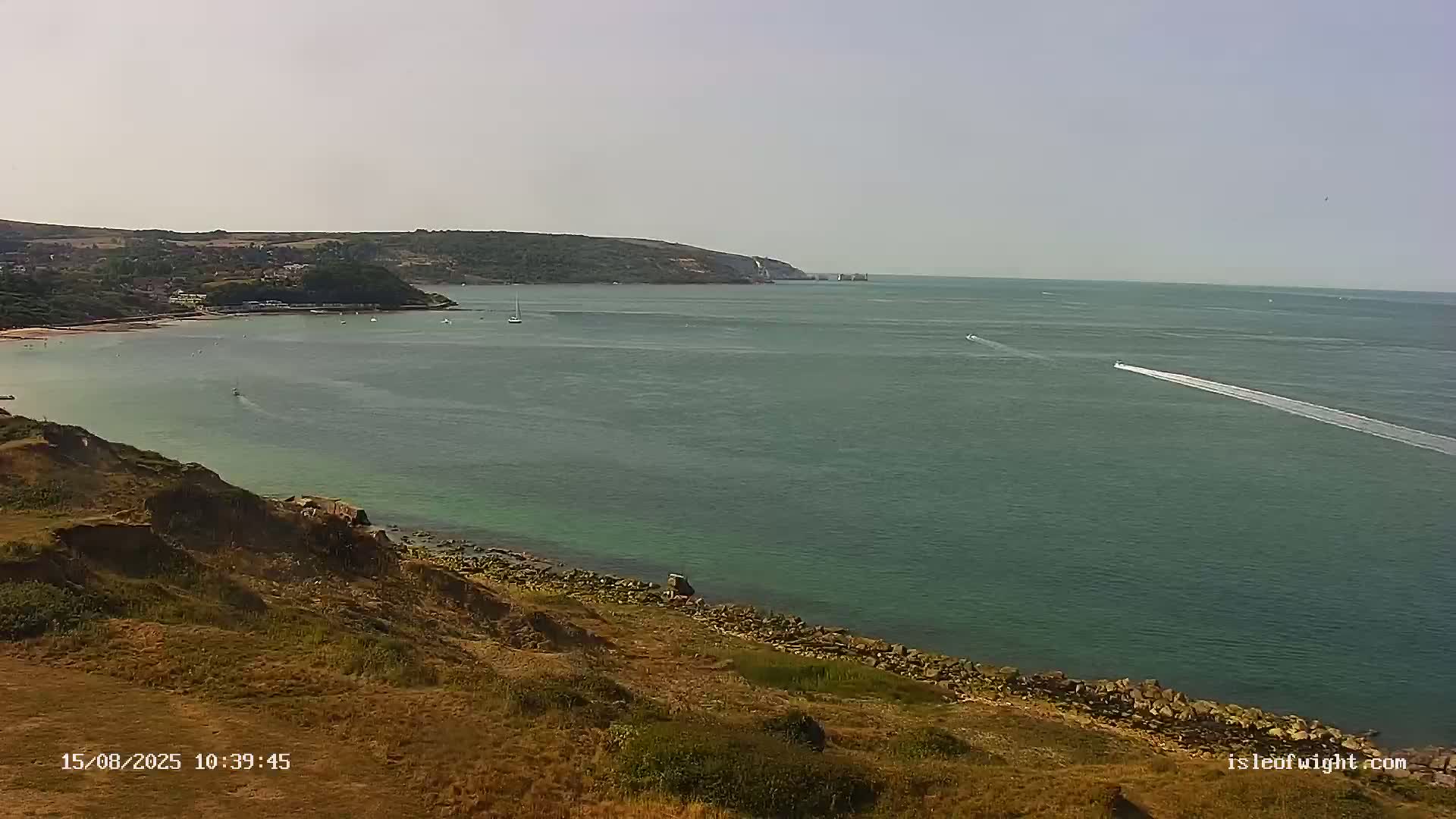 A calm, overcast day reveals a view of a wide body of water from a verdant clifftop.
