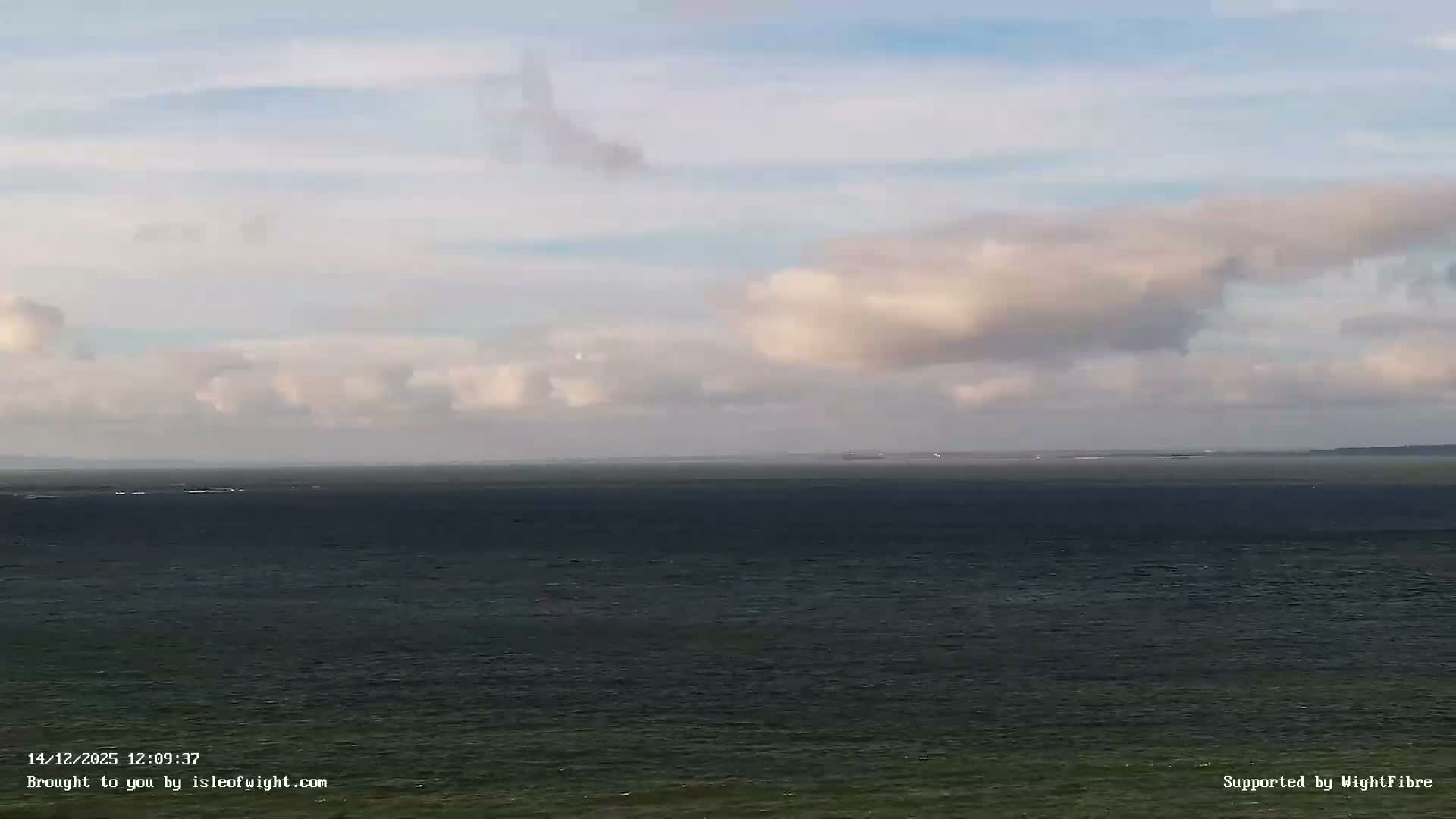 An overcast morning scene reveals choppy grey-green coastal waters, a rocky shore, and dark distant cliffs under a cloudy sky with faint golden light peeking through.