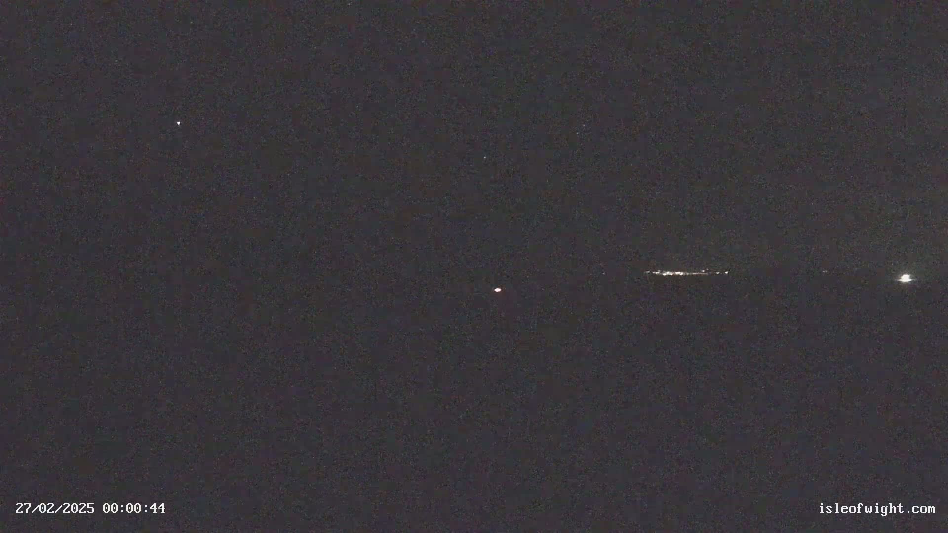 A nighttime long shot shows a faint reddish light in the center, a line of distant lights on the horizon, and a few brighter lights scattered across the dark sky.