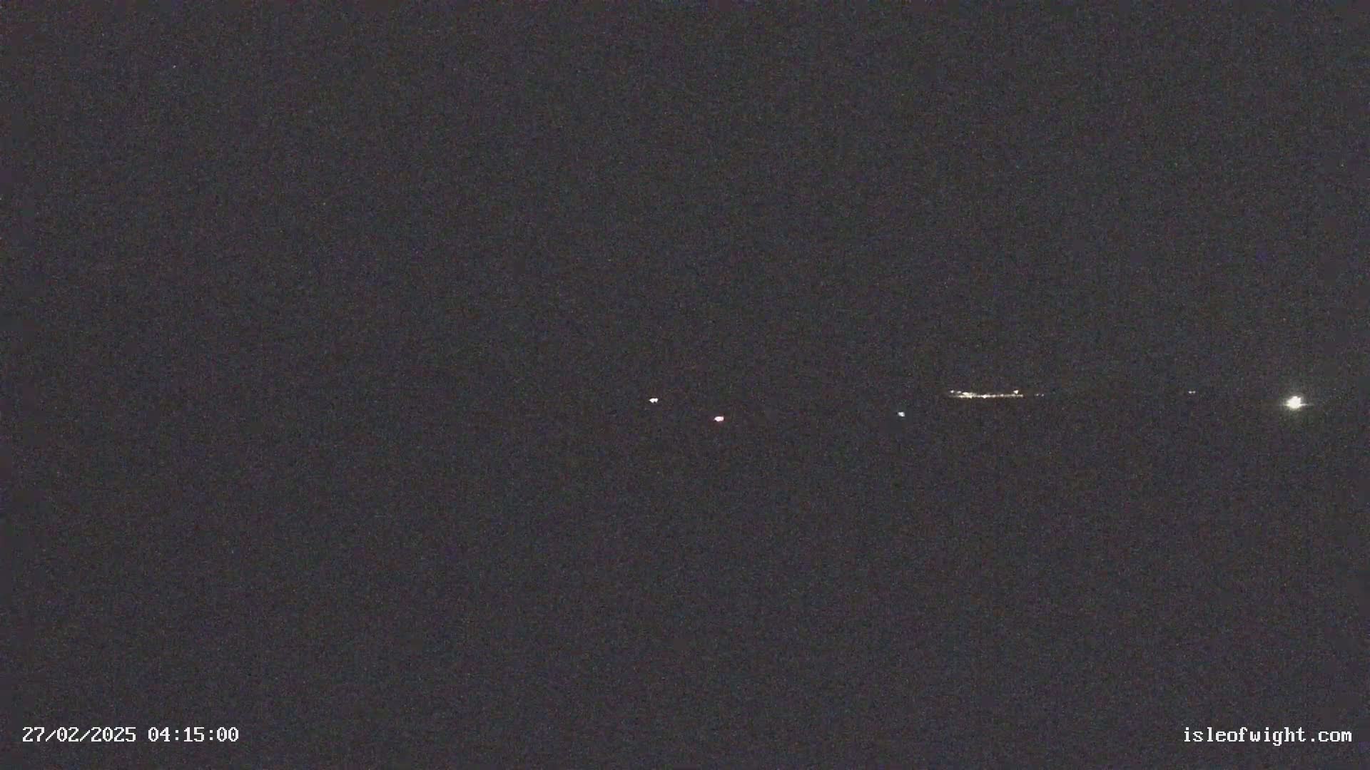 A dark, nighttime scene shows a few faint lights in the distance on the horizon.