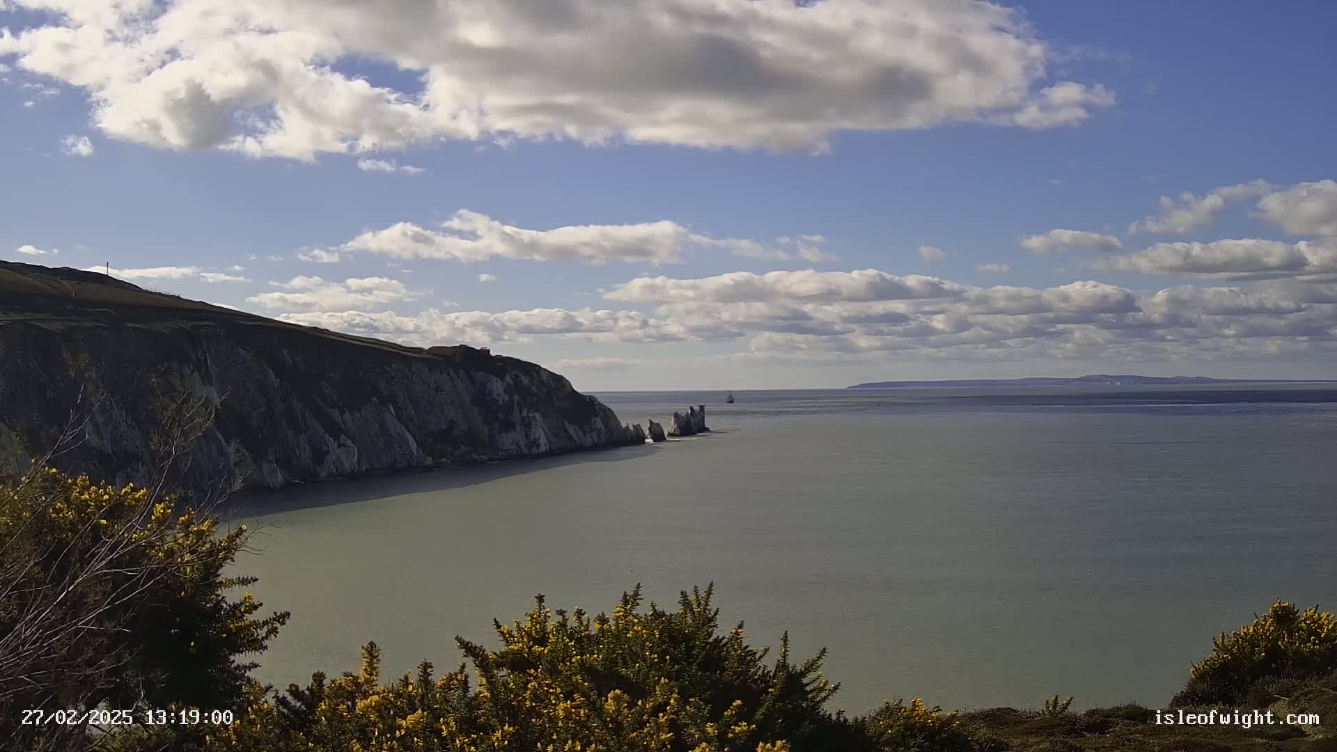 White cliffs meet a calm, grey sea under a partly cloudy sky, with a distant landmass visible on the horizon.