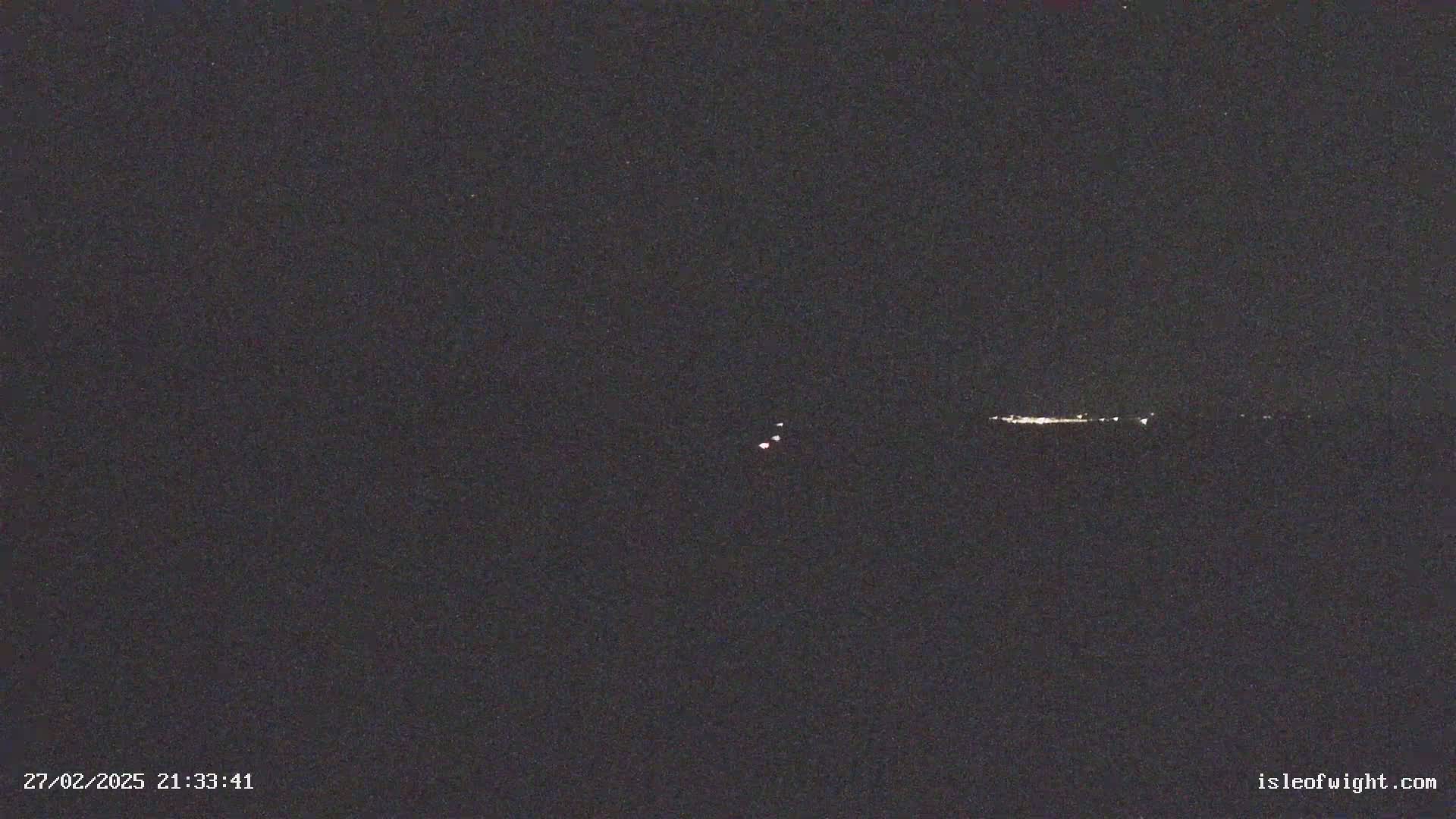 A nighttime, dark image shows a faint line of lights on the horizon and a few small, dim lights in the distance.