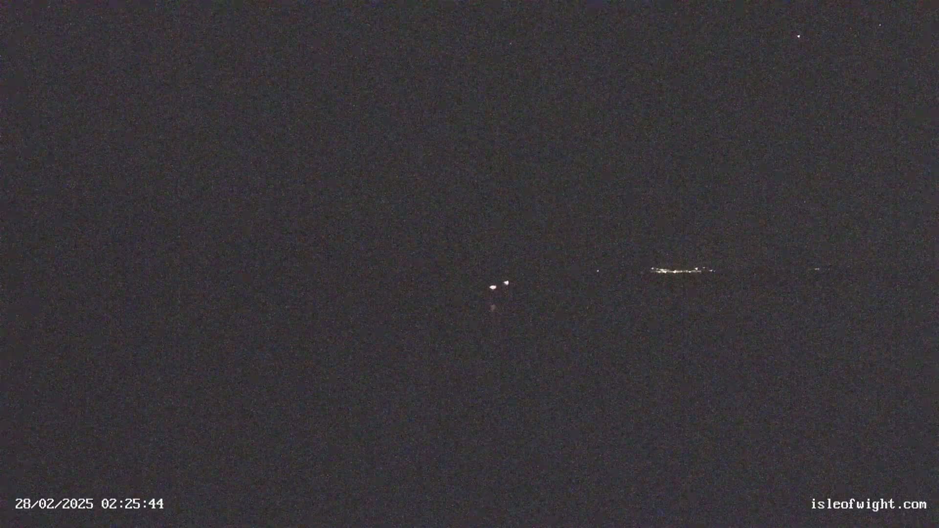 A dark nighttime scene shows a few faint lights in the distance on the horizon.