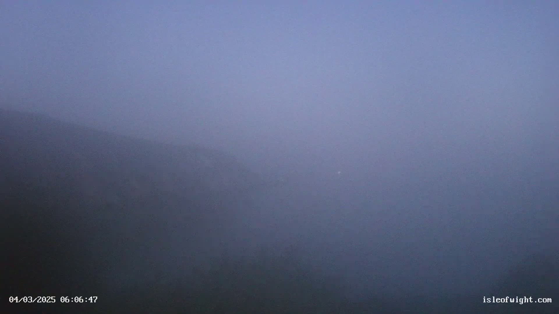 A foggy, dusky landscape shows a dimly lit hillside extending to the horizon under a pale purple sky.