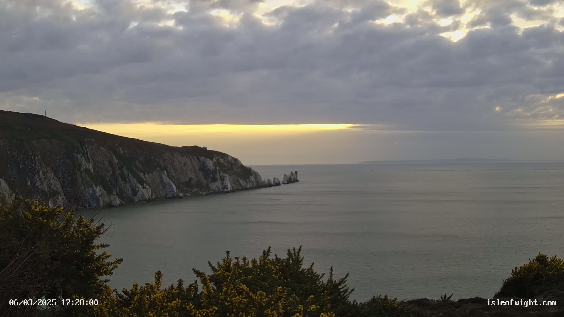White cliffs meet a calm sea under a partly cloudy sunset sky.