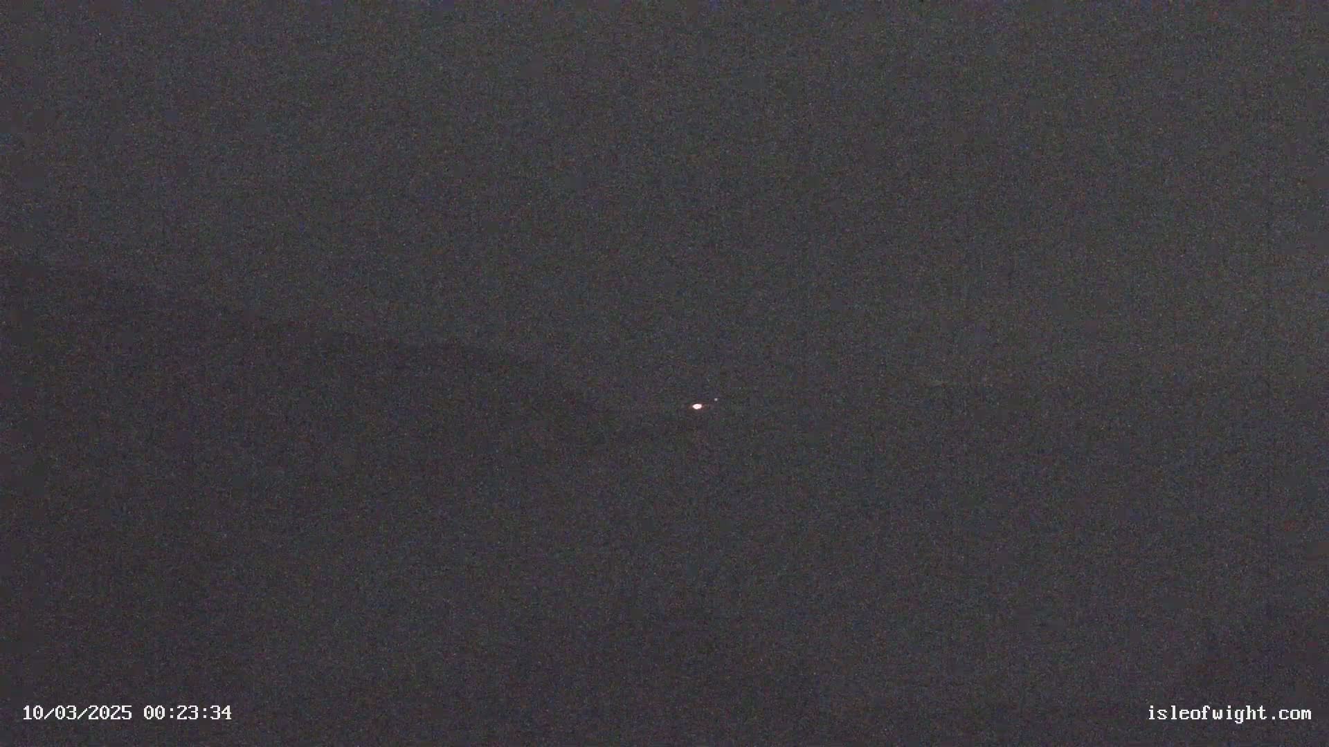 A small, faint, pinkish light is visible in a dark, night sky.