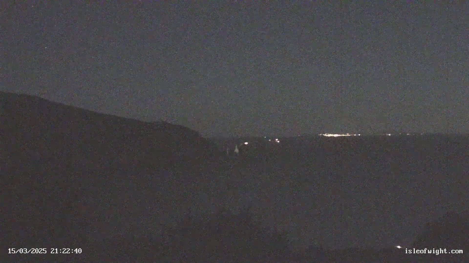 A dark, nighttime landscape shows a distant line of lights on the horizon under a clear, starless sky.