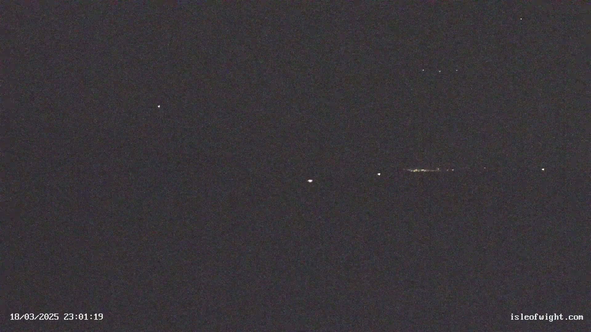 A nighttime long shot shows a few distant lights on the horizon under a dark, clear sky with visible stars.