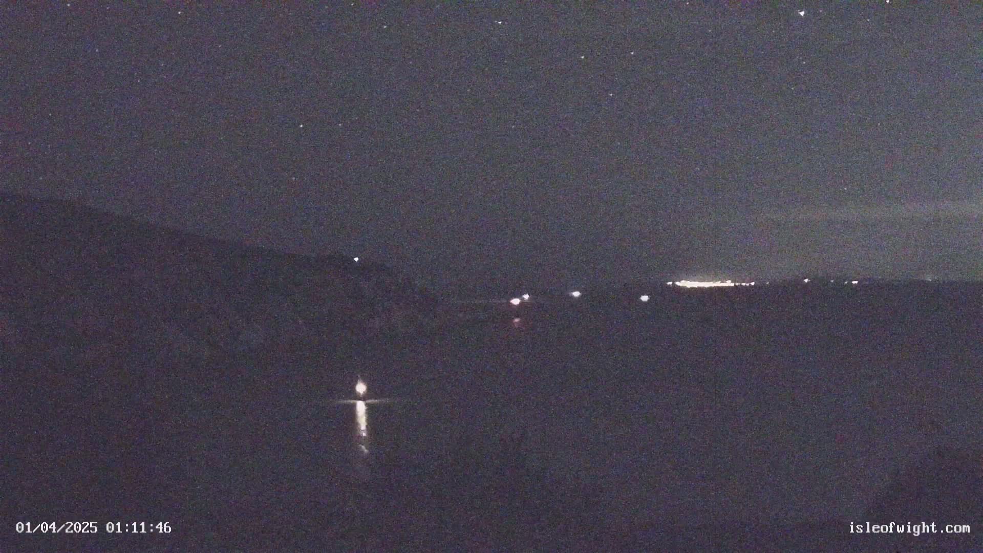 A nighttime long shot shows a dark landscape with a few faint lights in the distance under a starry sky.