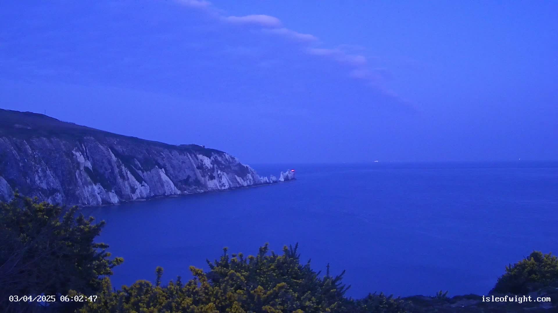 A dark-blue sea meets a white cliff face under a twilight sky.