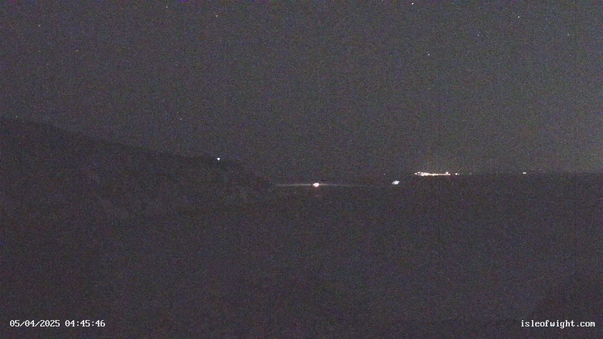 A dark, nighttime landscape shows a distant line of lights under a clear, starry sky.
