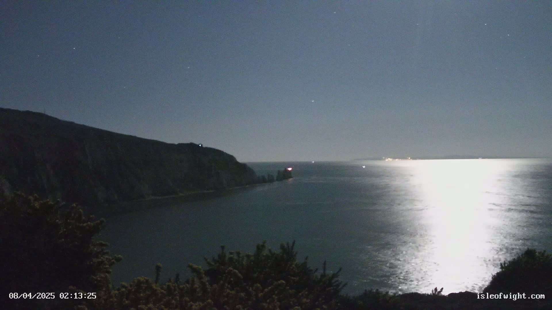 A moonlit night scene shows a dark, rocky shoreline and calm ocean waters reflecting the bright moonlight.