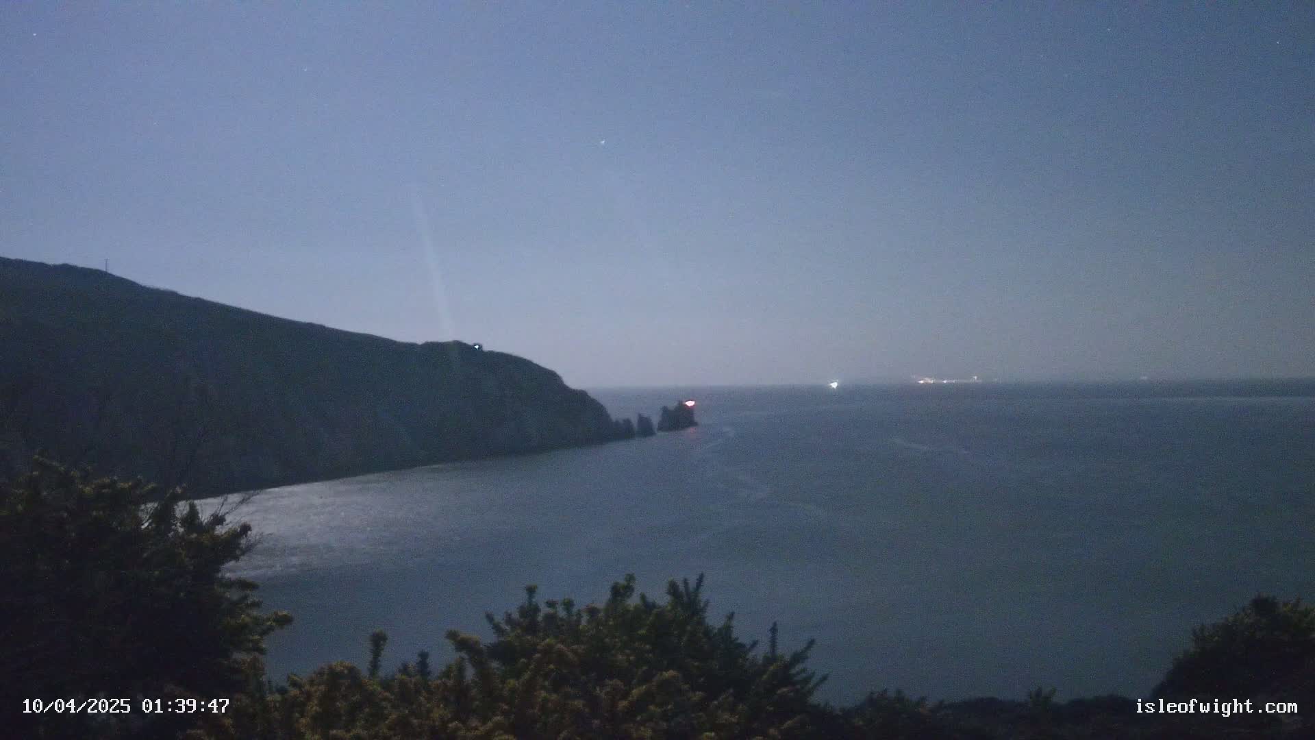 A dark, moonlit coastal scene shows a cliff overlooking a calm sea at night, with a faint light visible on a distant structure.
