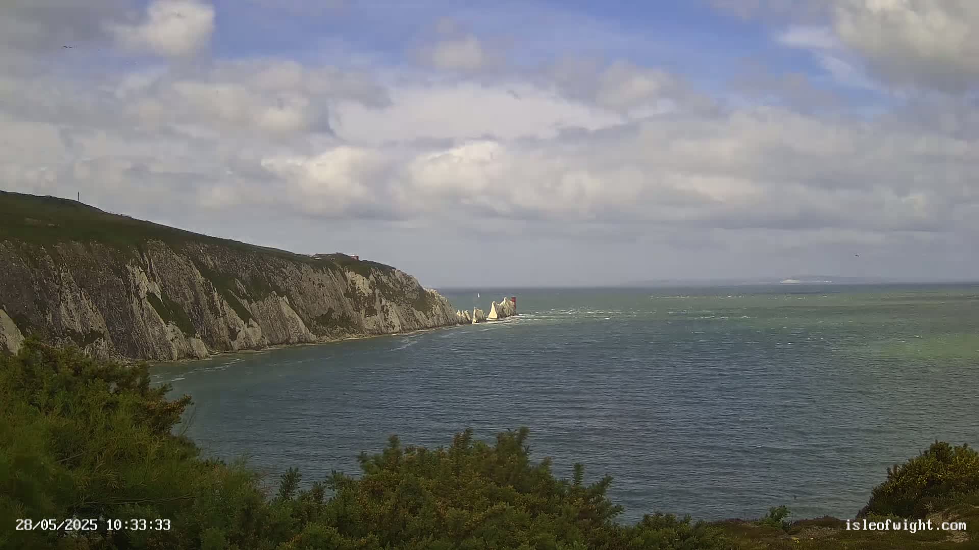 A partly cloudy day shows white cliffs and a body of water with a choppy surface.