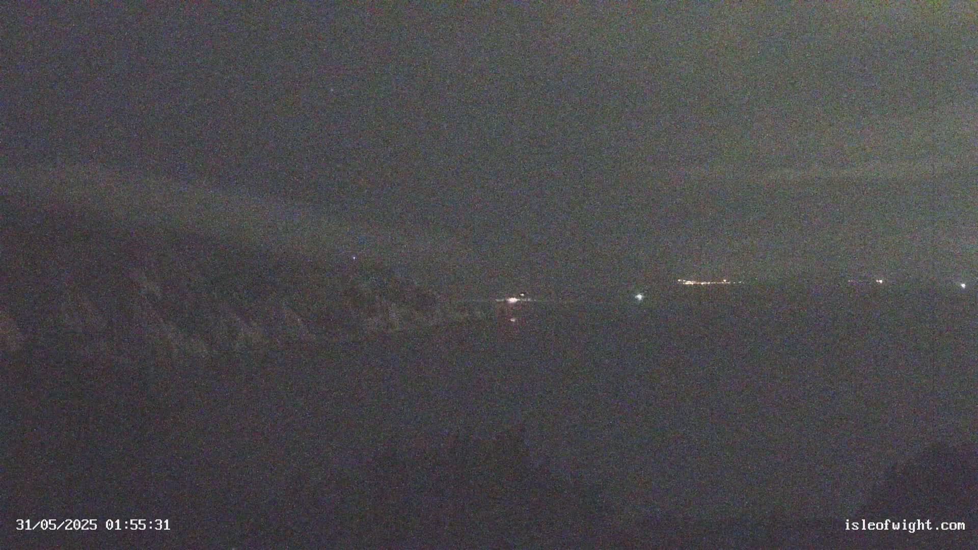 A dark, nighttime view shows a distant shoreline with faint lights under a mostly clear sky.