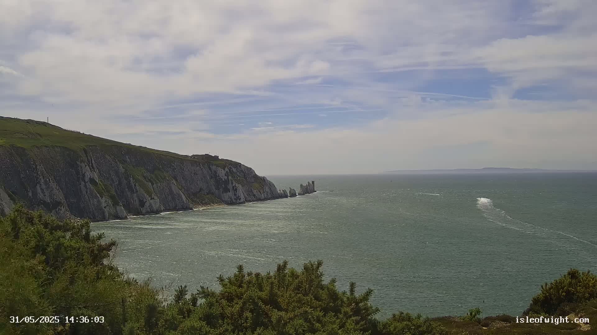 White cliffs meet a calm, gray-green sea under a partly cloudy sky.