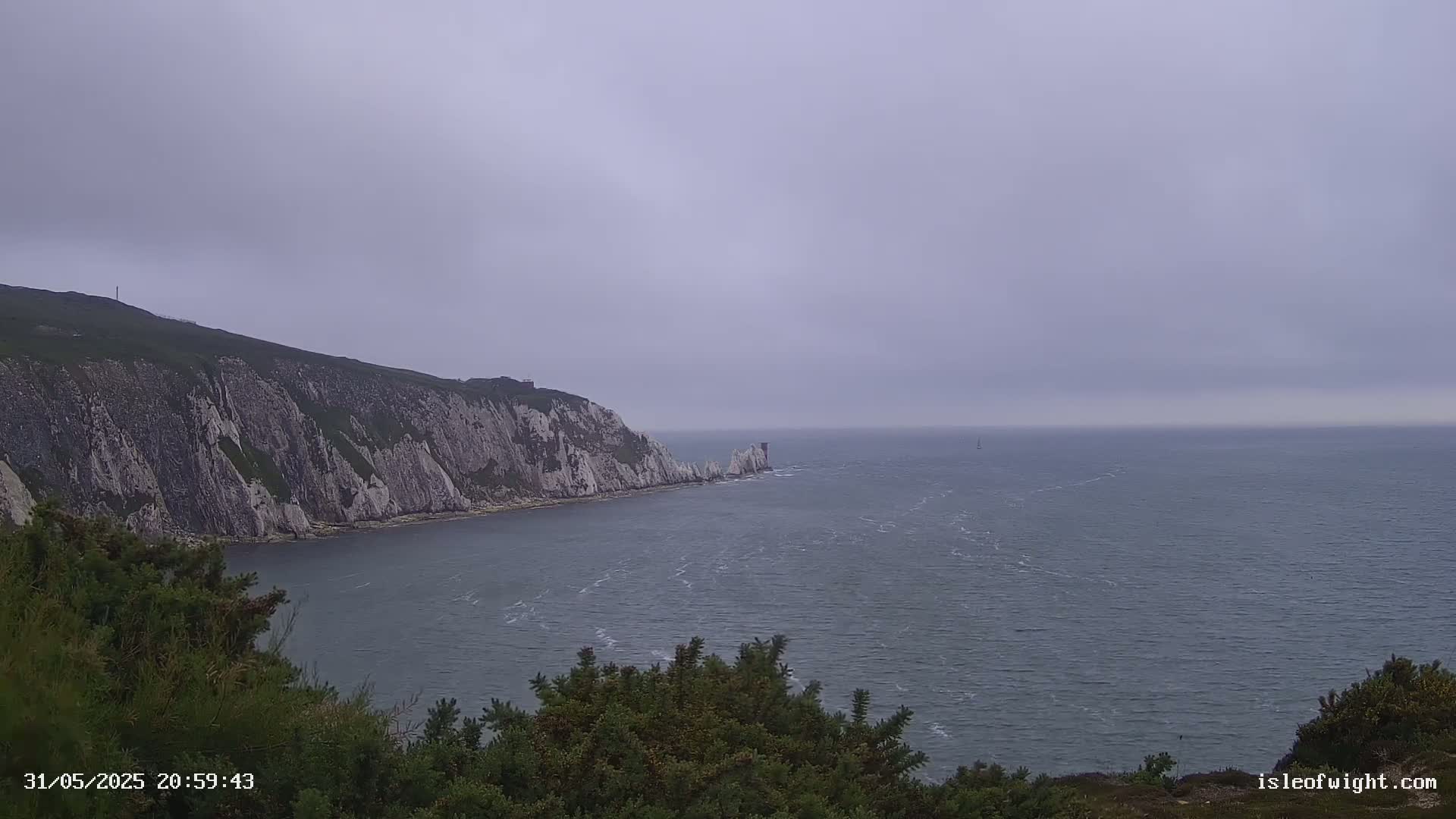 A view of a rocky, white cliffside overlooking a calm, gray sea under an overcast sky.