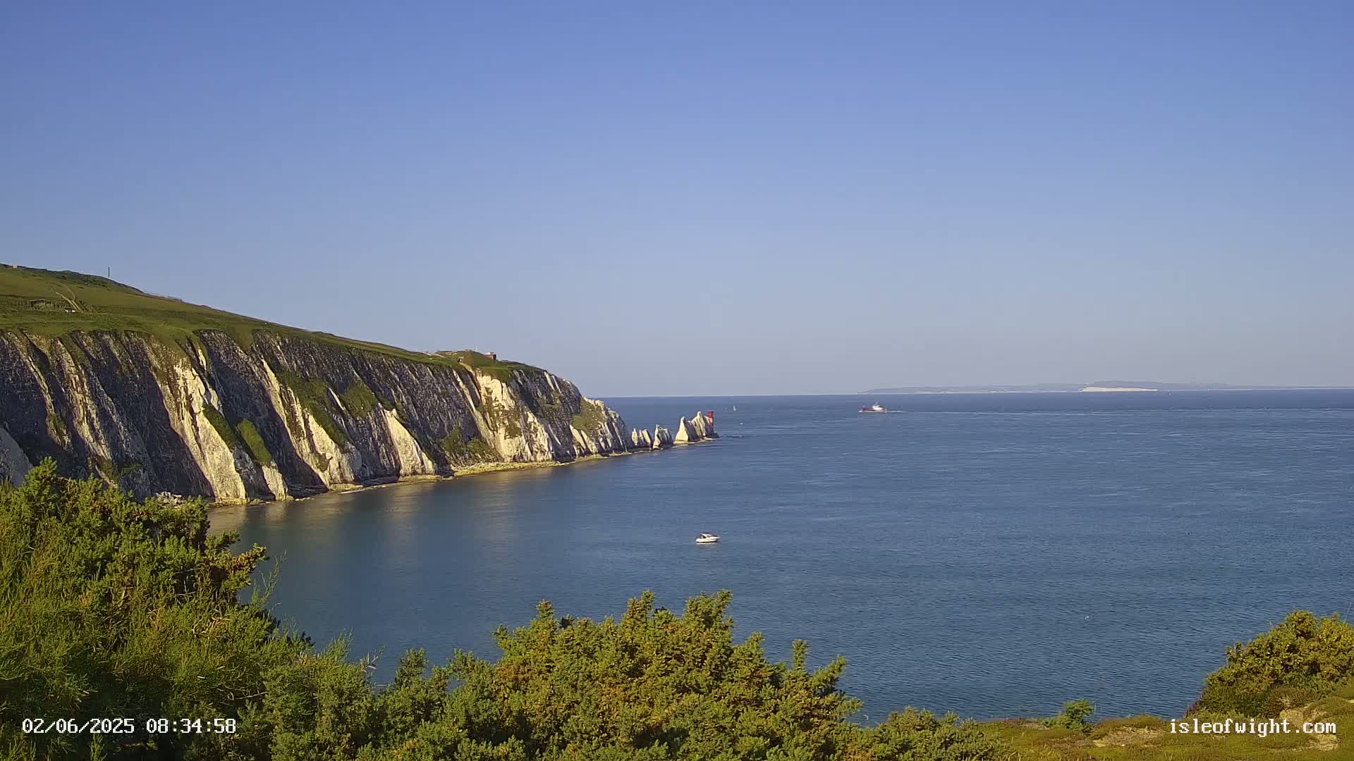 White cliffs meet a calm, blue sea under a clear, sunny sky, with a small boat visible on the water.