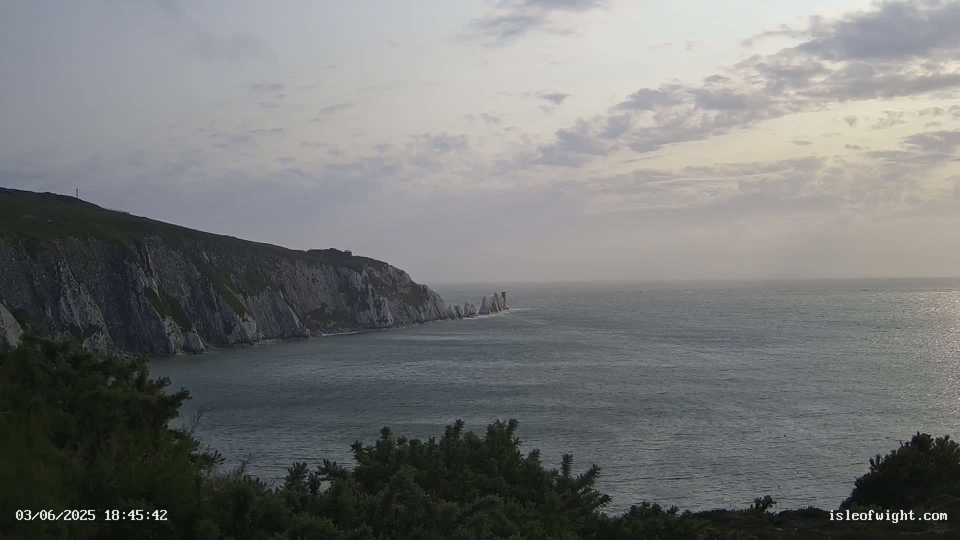 White cliffs meet a calm, gray sea under a cloudy sky.