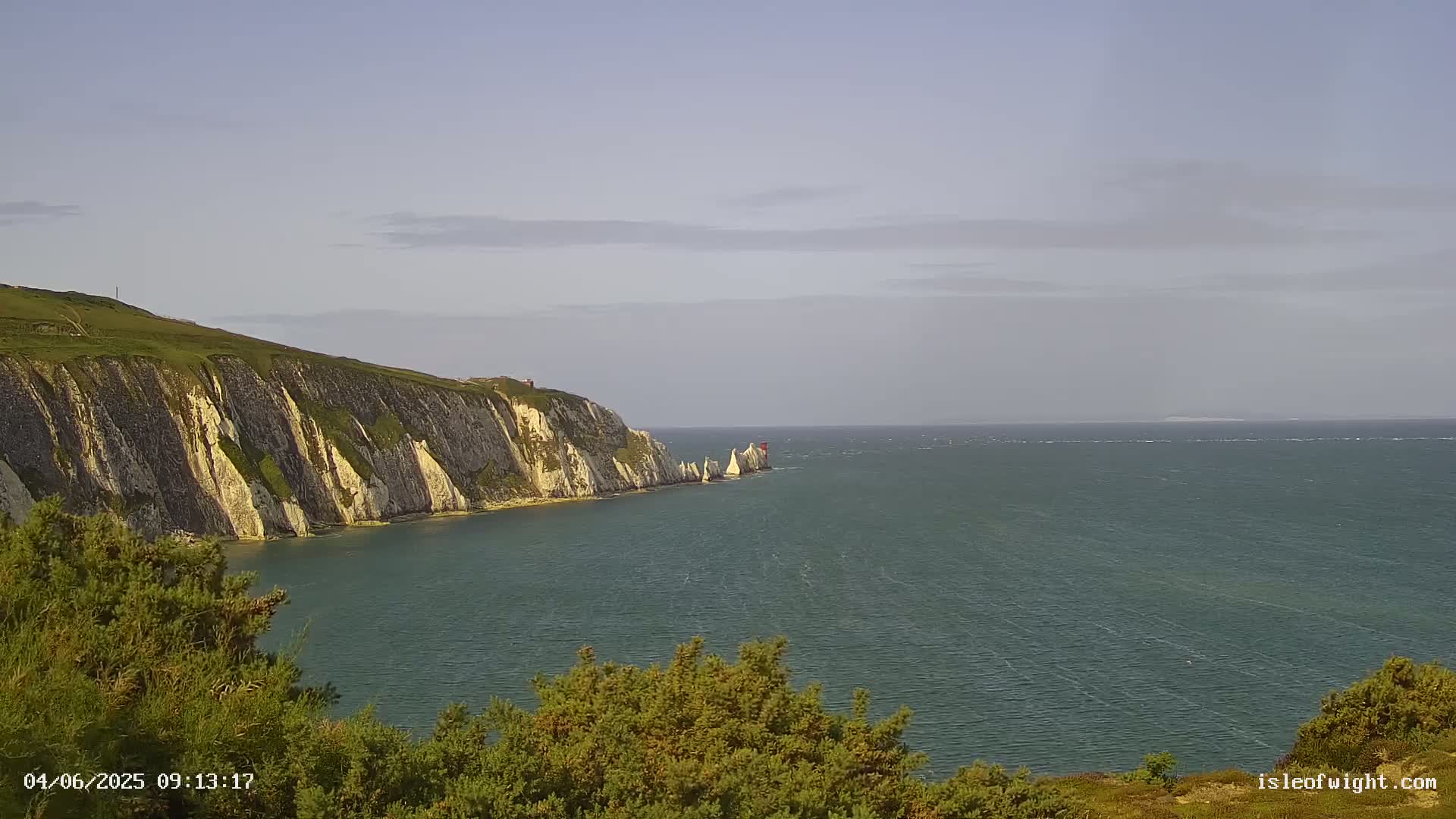 White cliffs meet a calm, somewhat hazy sea under a pale sky.