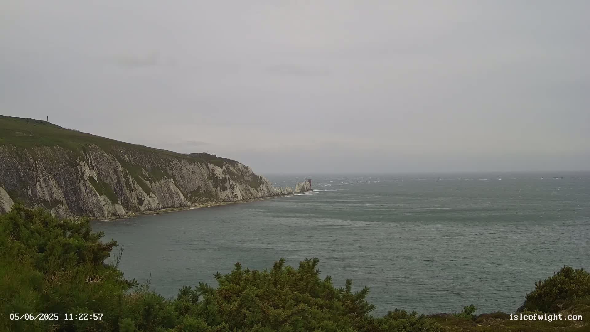 A view of a steep, white cliff face along a dark-grey, choppy sea on an overcast day.