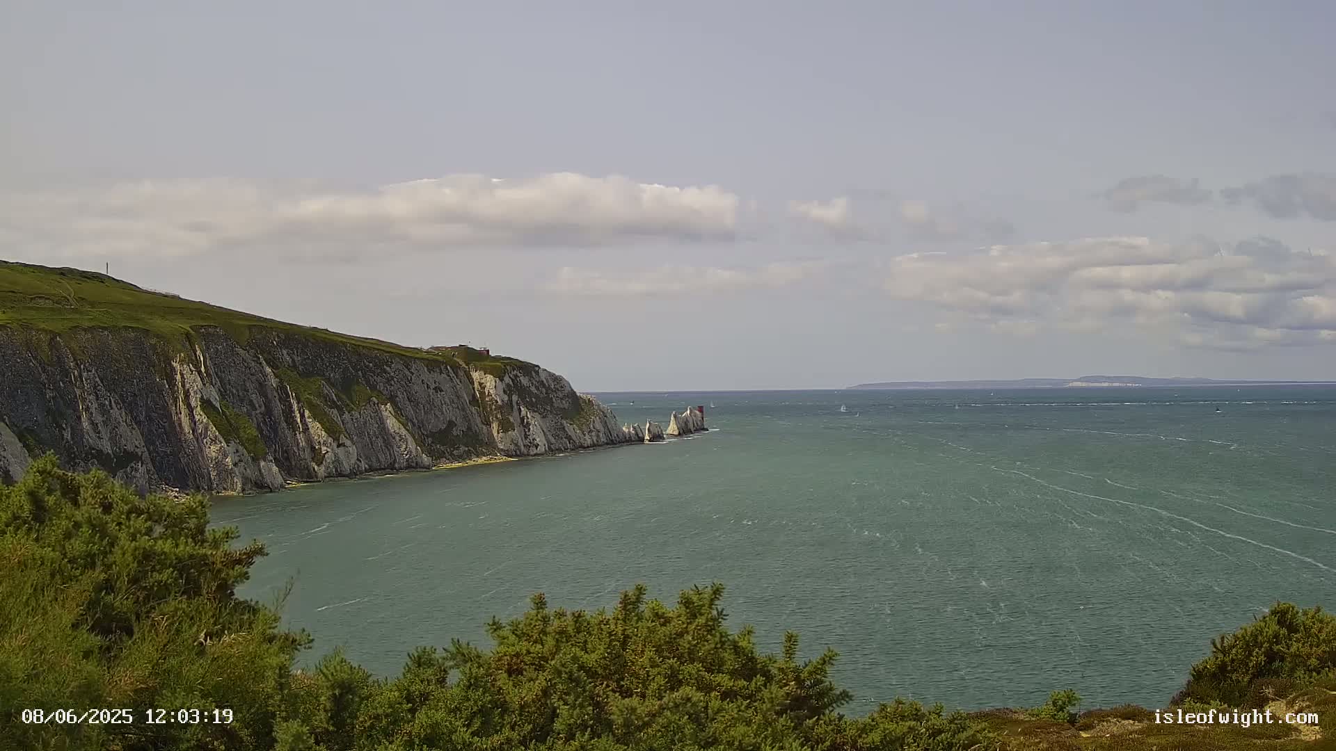 White cliffs meet a green-blue sea under a partly cloudy sky.
