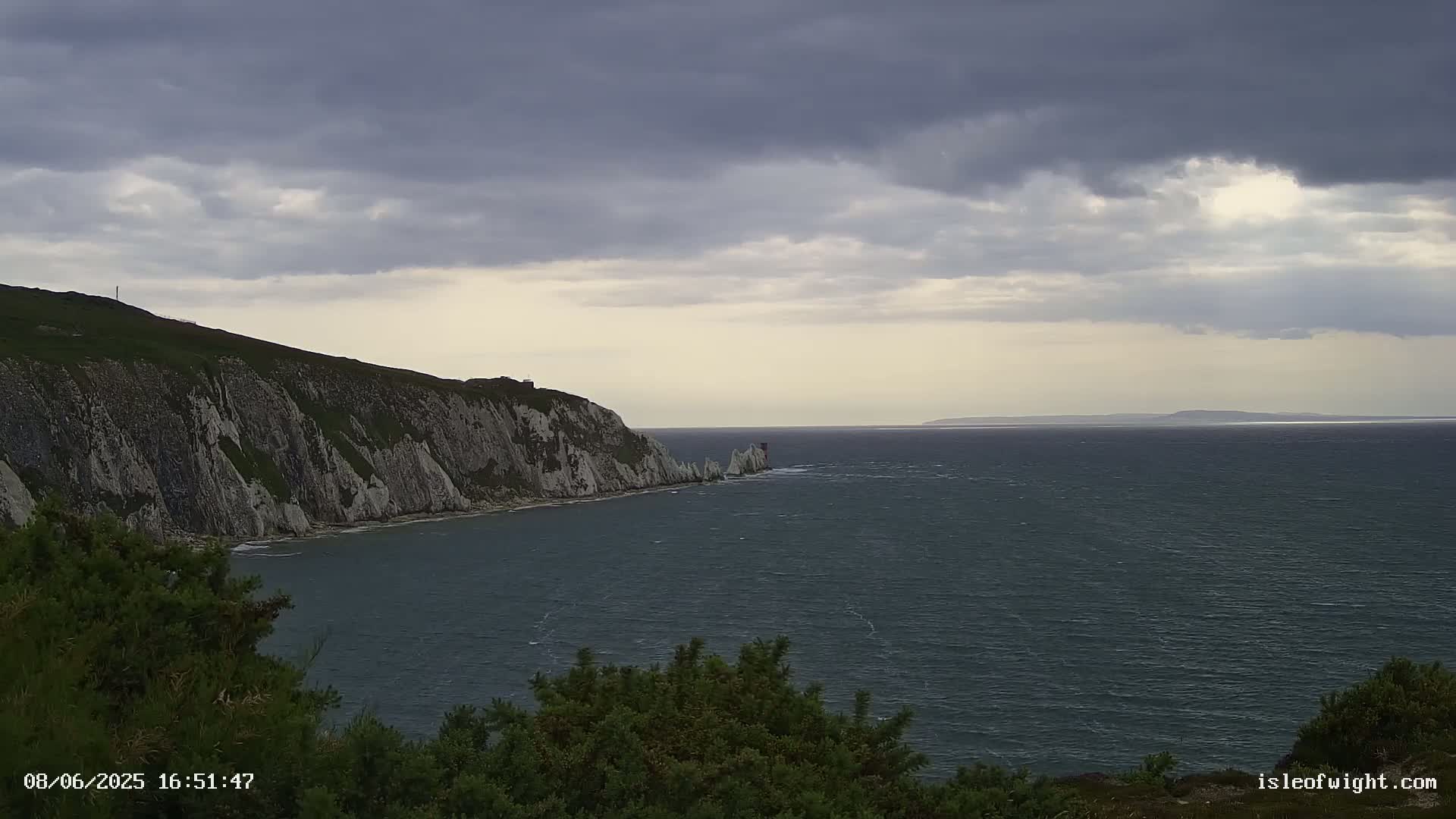 White cliffs meet a dark, choppy sea under a cloudy sky, with a distant landmass visible on the horizon.
