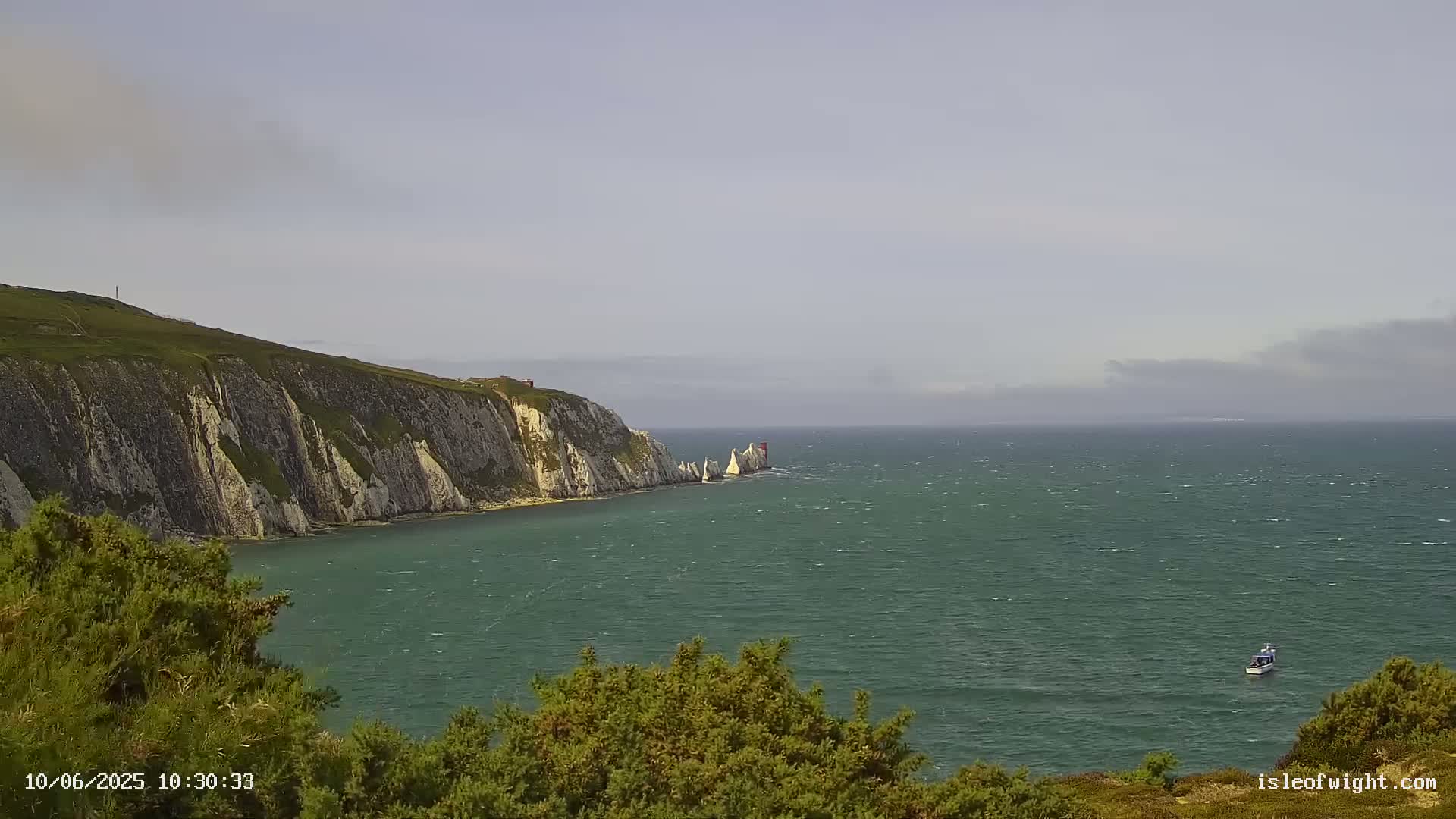 White cliffs meet a green-blue sea under a mostly clear sky with some clouds on the horizon, a small boat visible in the distance.