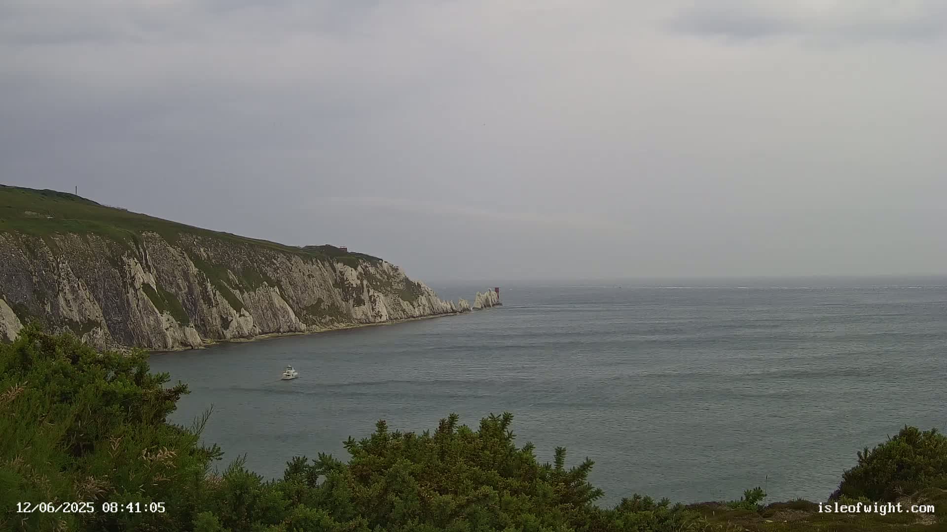 A boat is visible on a calm, gray day in the sea near a white cliffside.