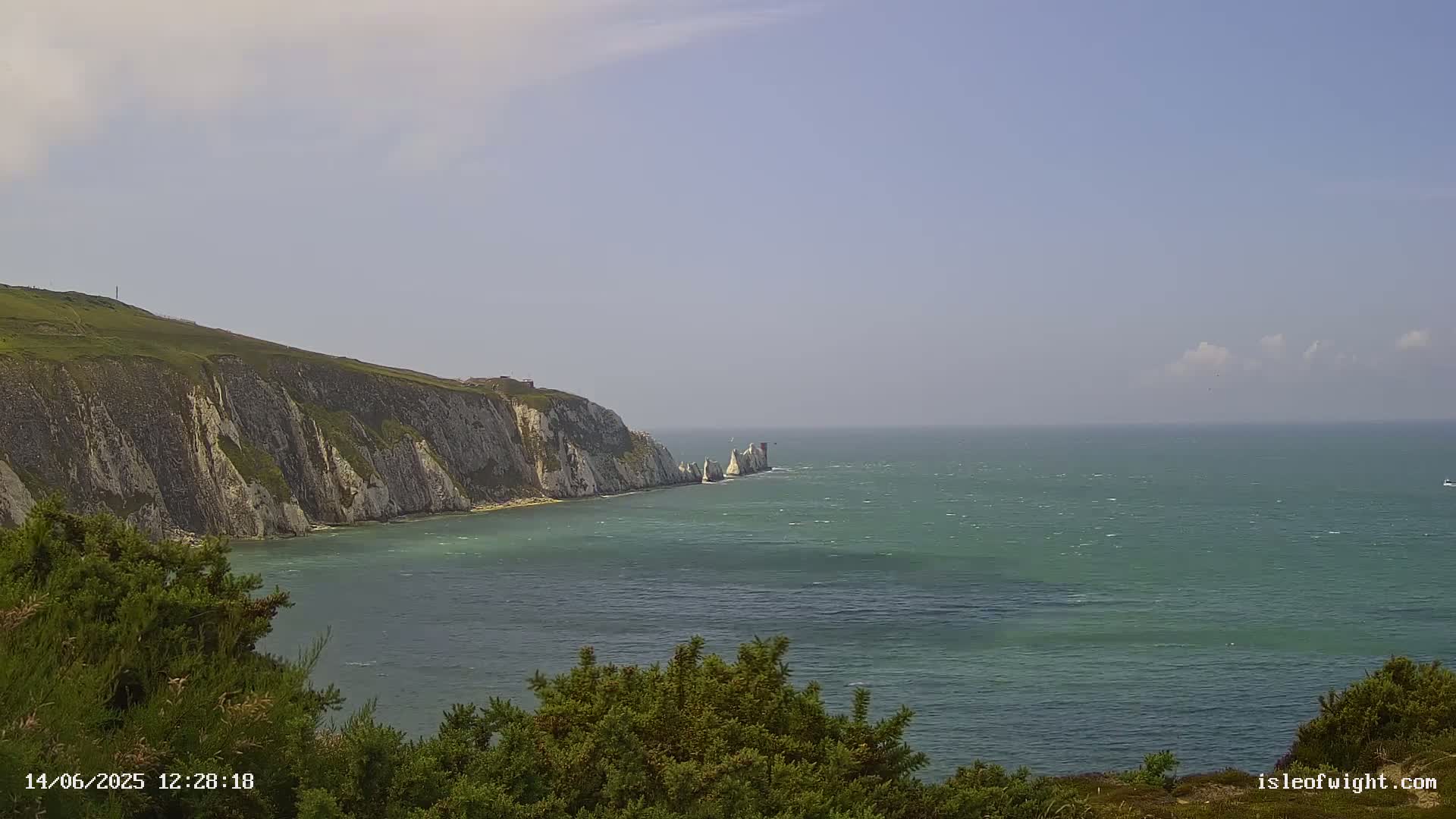 White cliffs and sea stacks rise from a green-blue sea under a mostly clear sky with a few clouds.