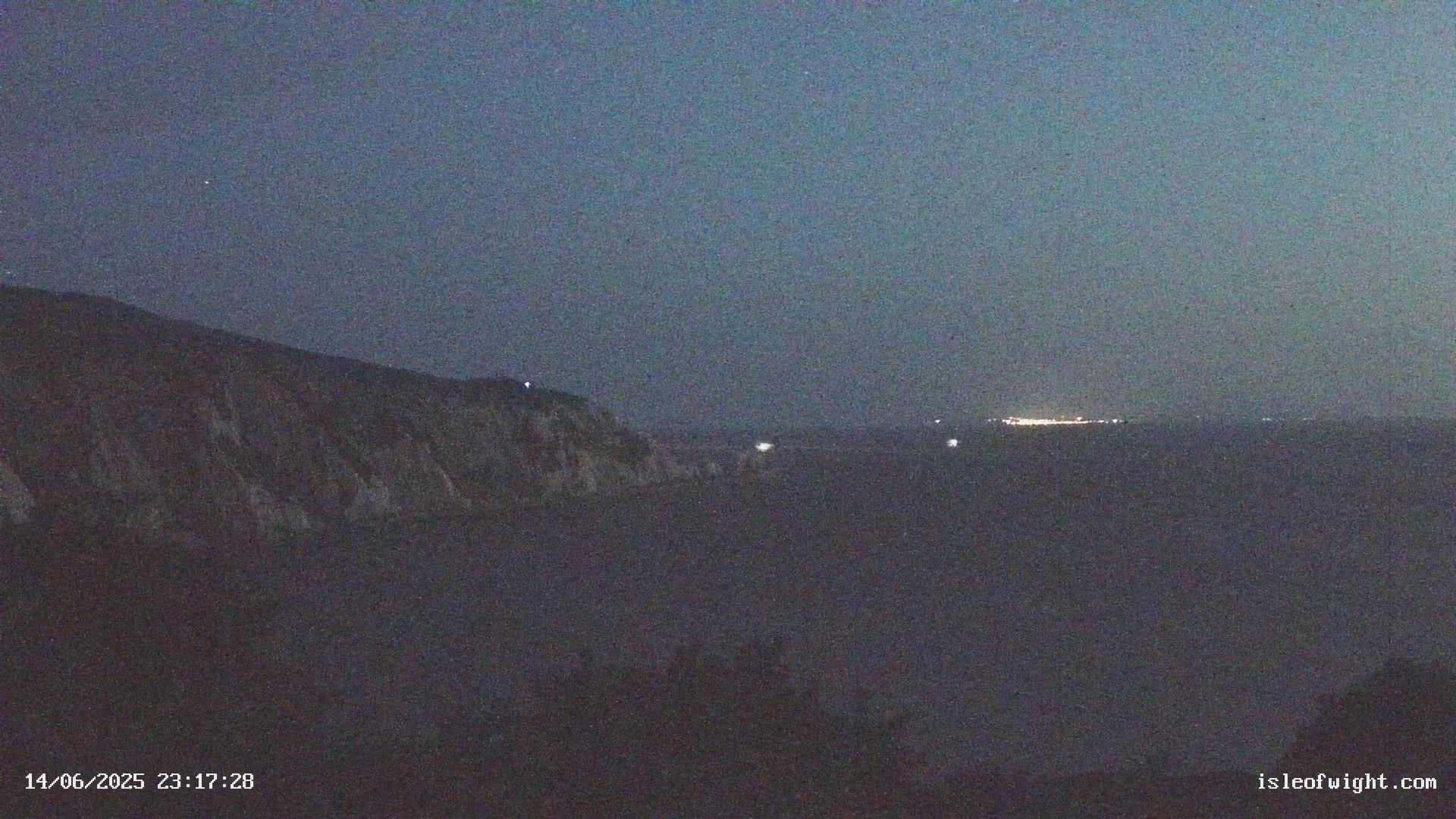 White cliffs rise from a calm, sunlit sea, with a line of smaller rock formations visible further out.