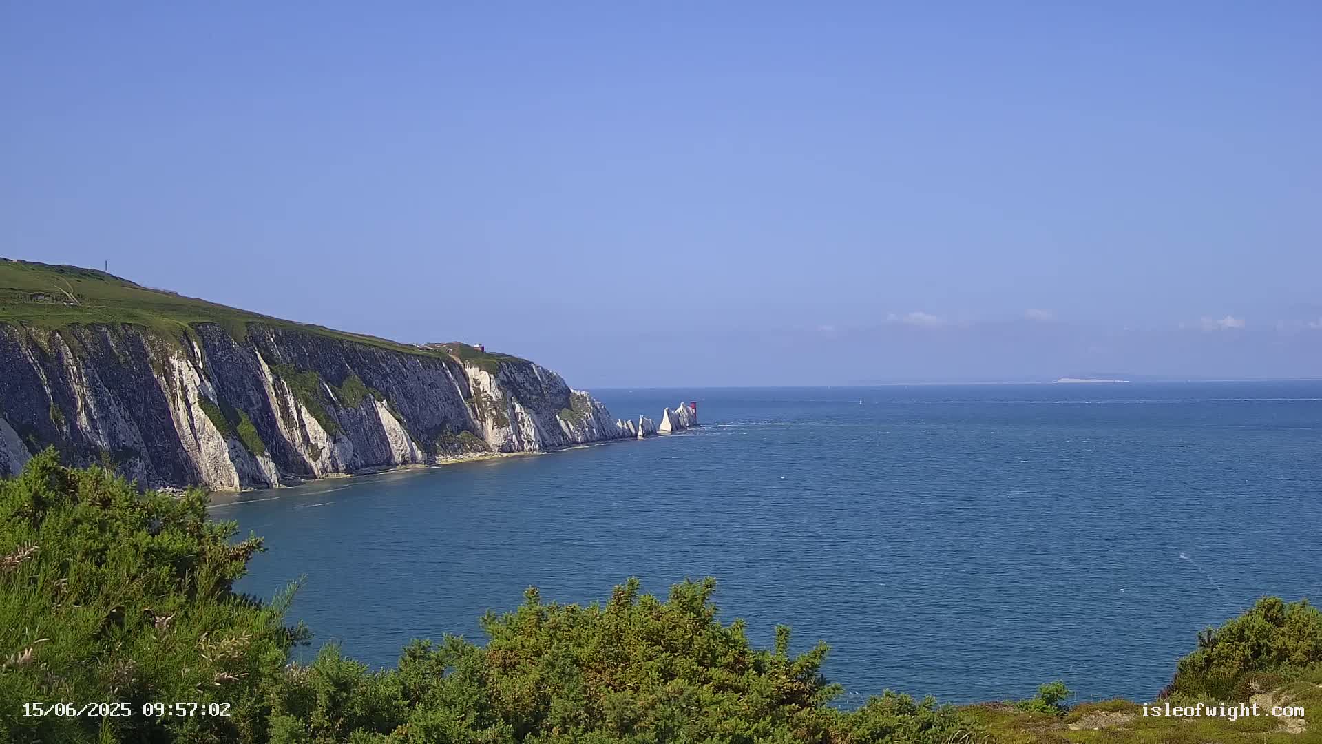 White cliffs rise from a calm, blue sea under a clear blue sky.