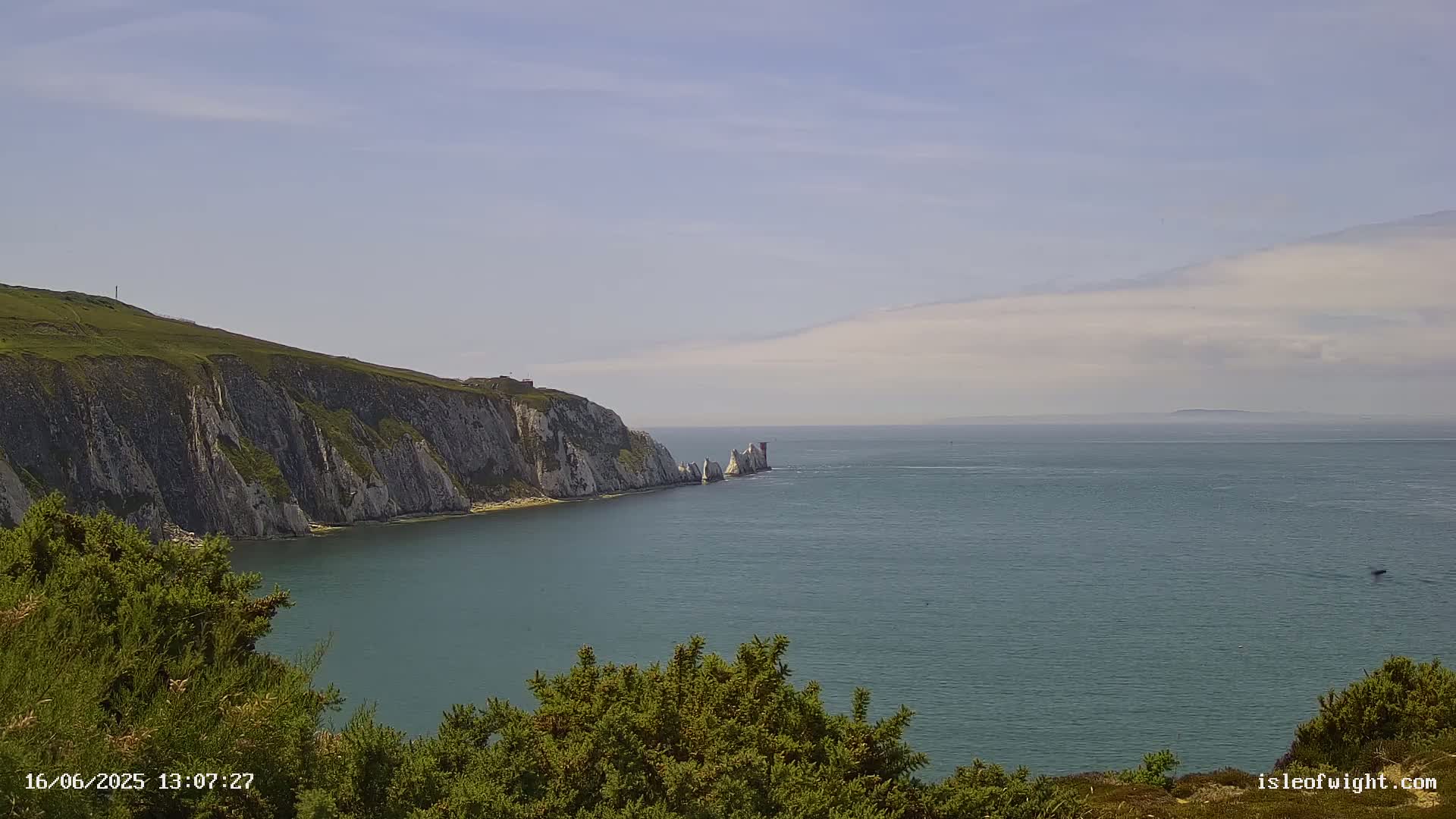 White cliffs and a line of sea stacks rise from a calm, blue sea under a mostly clear sky.