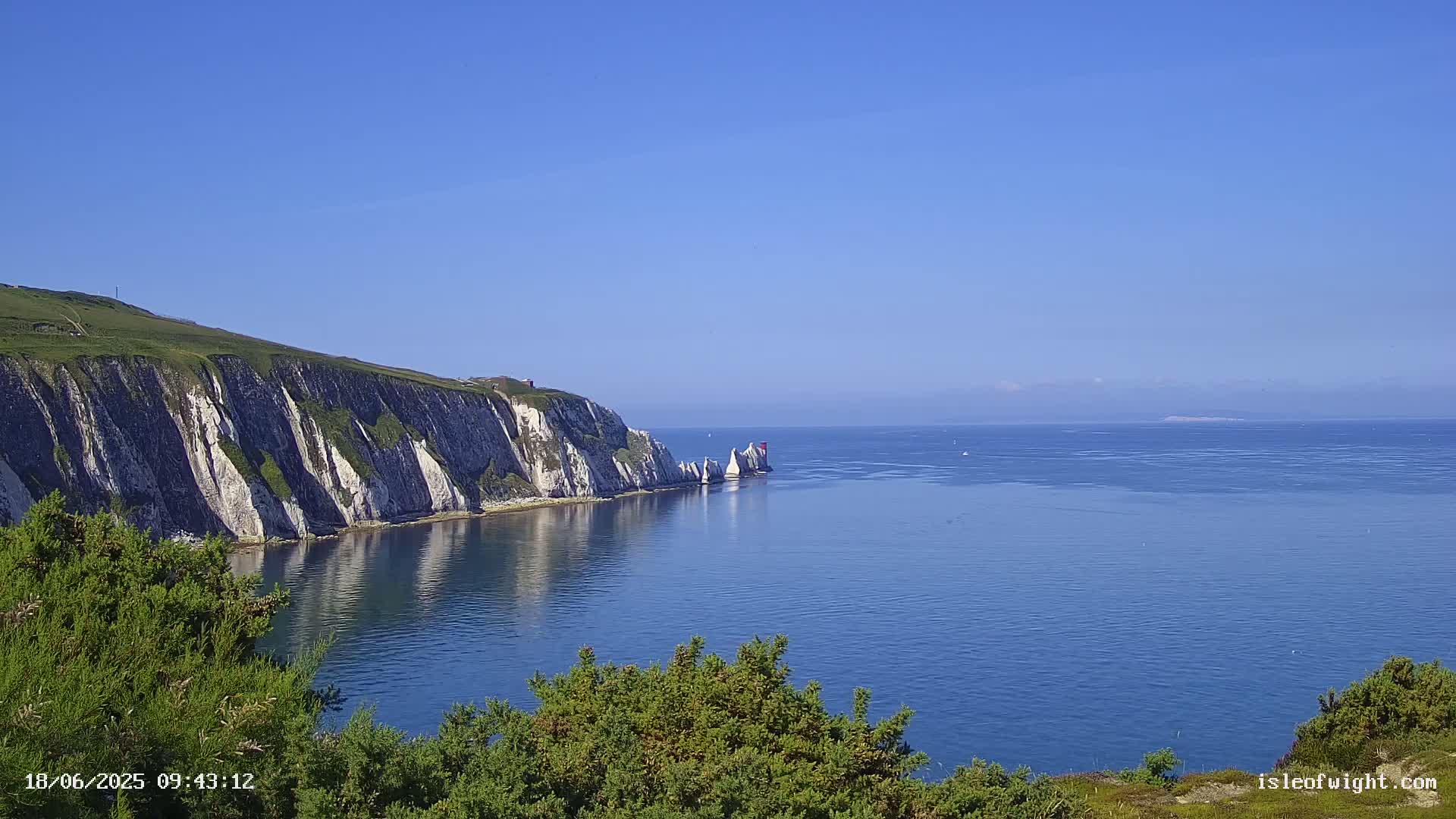 White cliffs rise from a calm, blue sea, with several prominent rock formations visible in the water.